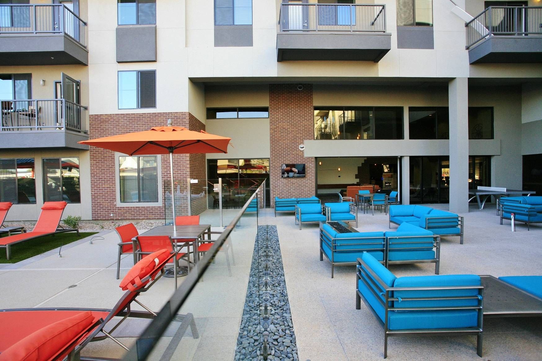 A vibrant outdoor courtyard at Alta Steelyard Lofts with red sun loungers, blue sofas, and an orange umbrella.