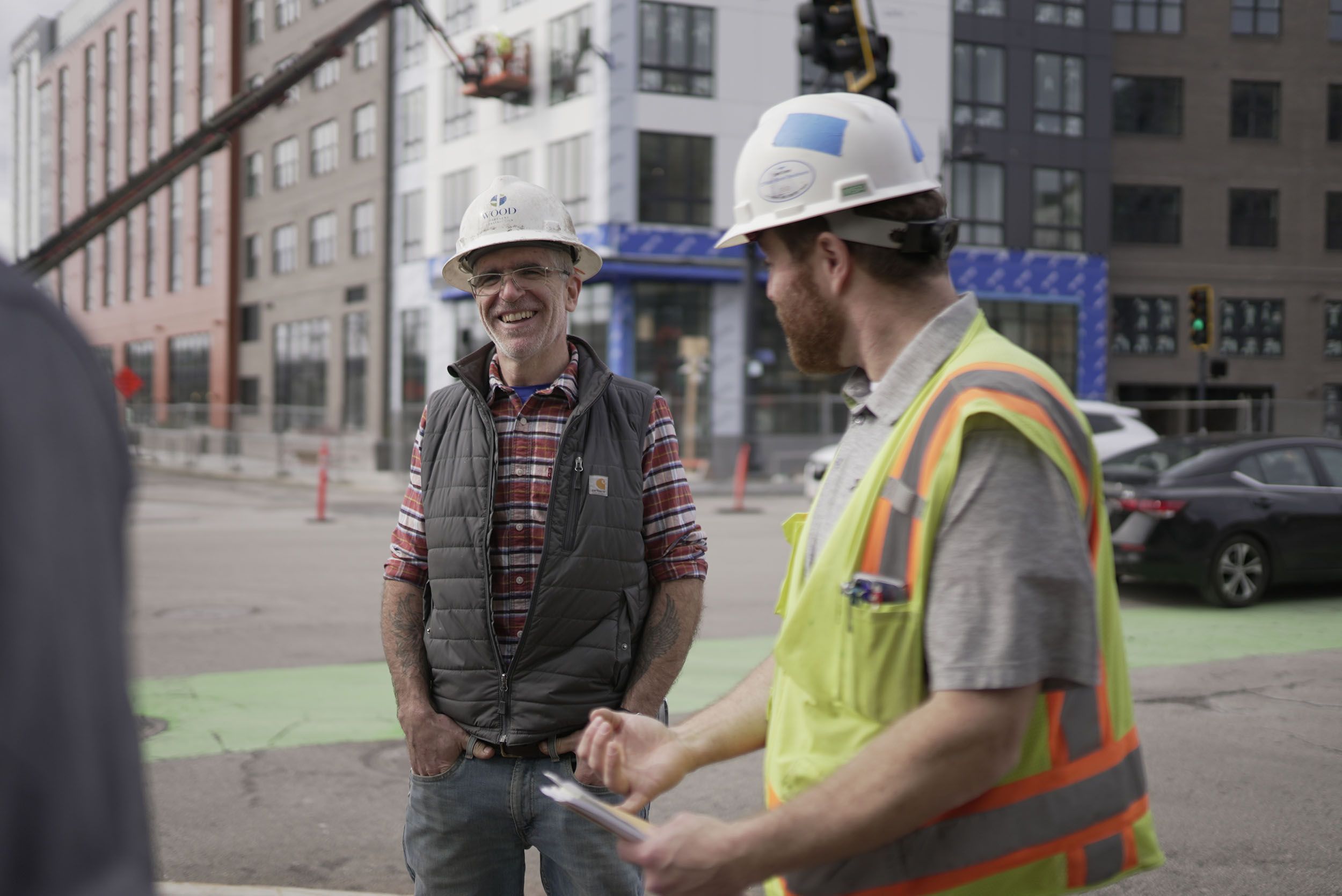 Two men in hard hats working on construction site talking and smiling.