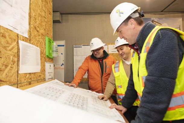 A construction team reviews blueprints together in a small room