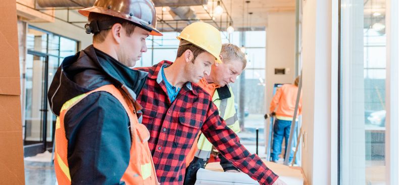 Group of construction workers review a set of plans on a table.