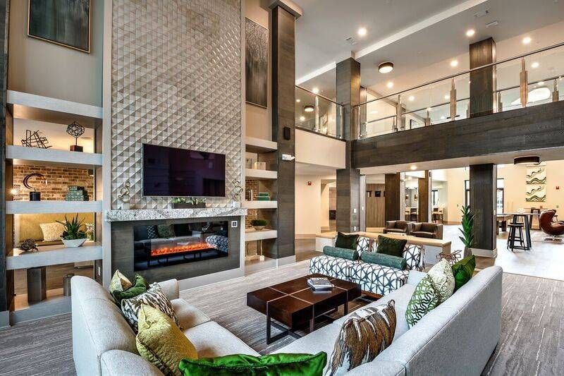 A modern clubroom featuring a fireplace with a tile surround, a two-story ceiling, and comfortable seating areas at Alta at Jonquil.