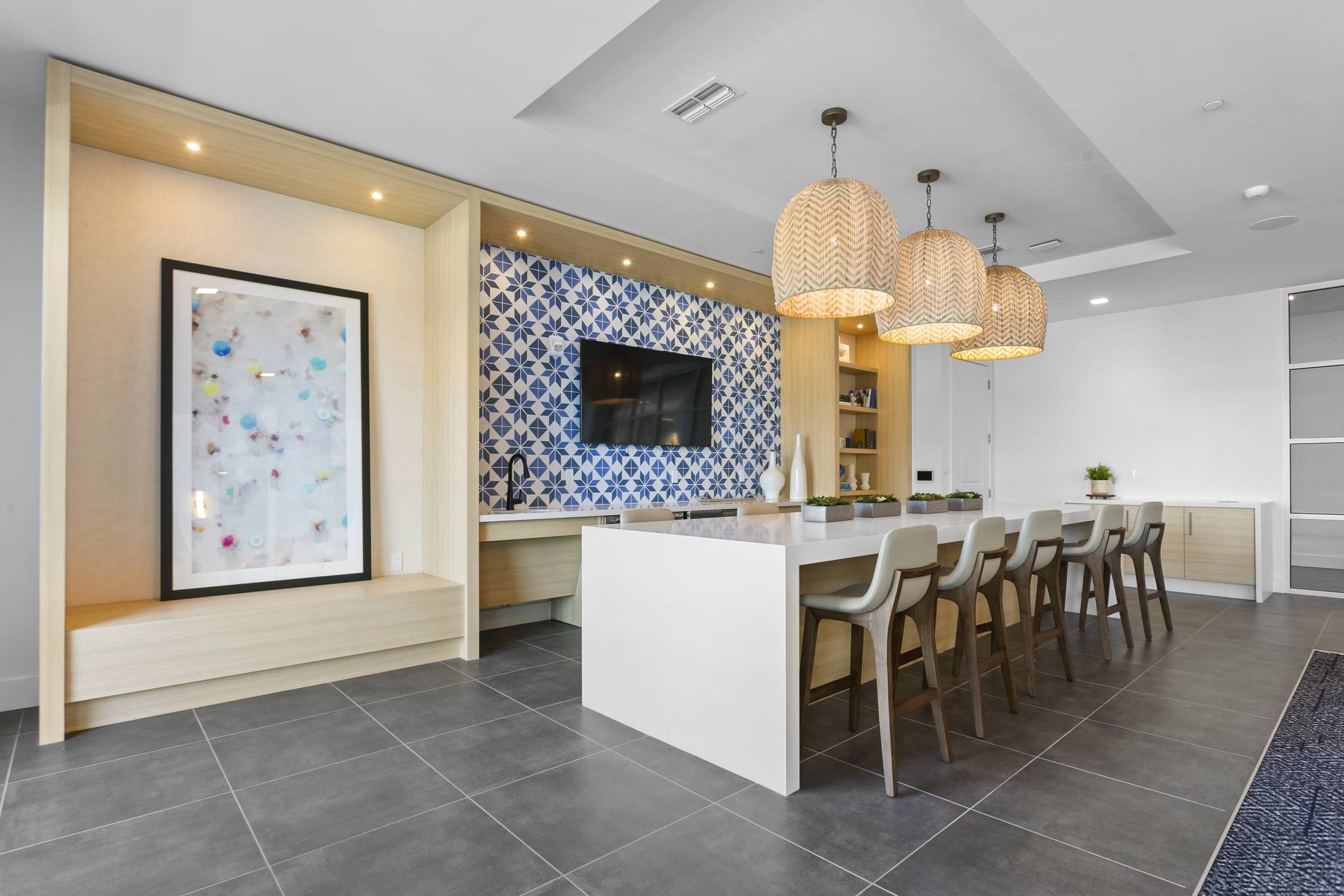 Inside the Alta Belleair clubhouse, a stylish kitchen bar is adorned with unique blue patterned tiles and elegant pendant lights, complemented by a contemporary art piece.