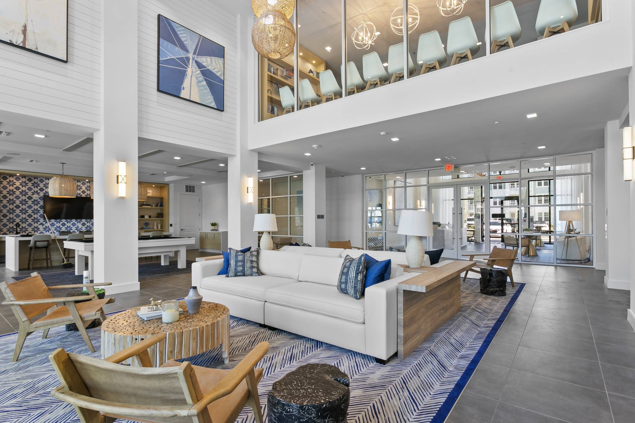 Alta Belleair's luxurious club room exudes comfort with its modern furnishings, vibrant blue accents, and an open-concept kitchen in the background.