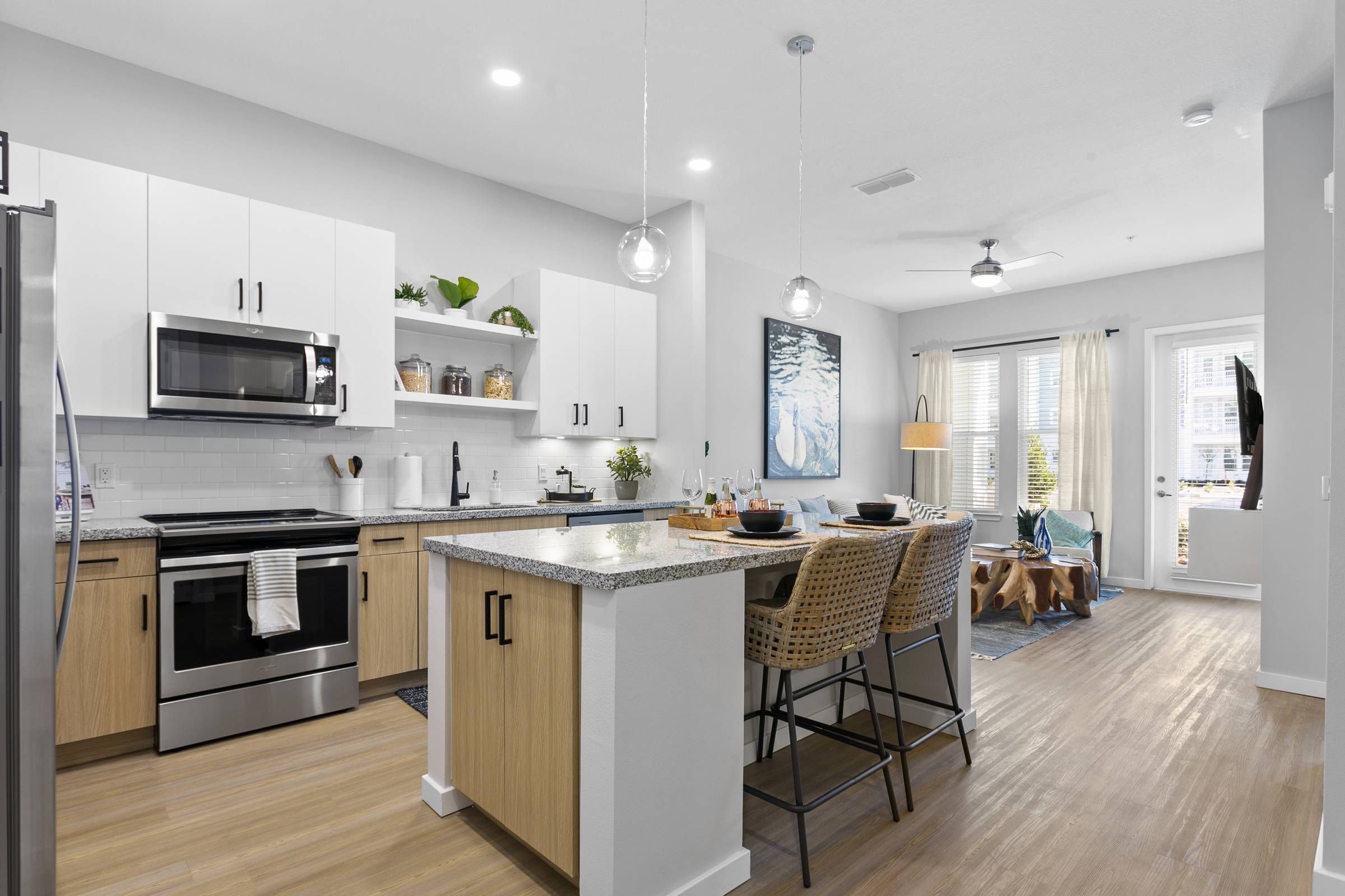 A sleek, modern kitchen inside Alta Belleair with white cabinetry and stainless steel appliances, overlooking a cozy living area with abundant daylight.