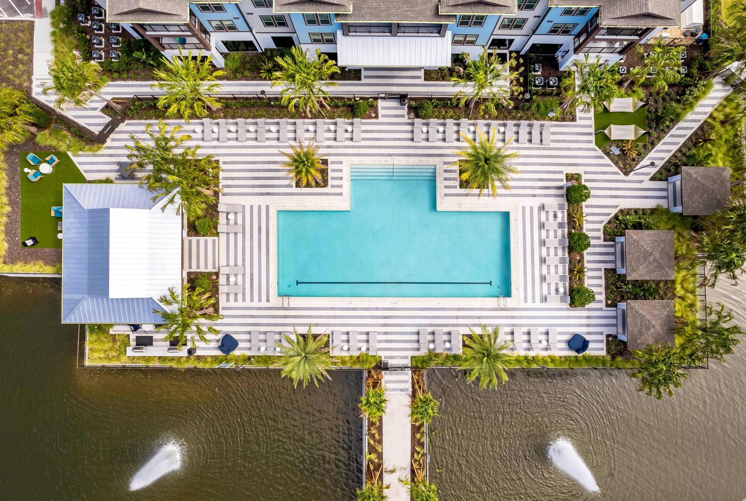 Overhead view of Alta Clearwater's luxurious pool area, bordered by palm trees and symmetrical sun loungers, with water features adding to the tranquility.