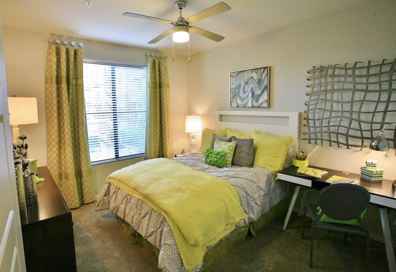A cozy, well-lit bedroom at Alta Steelyard Lofts with yellow bedding, green curtains, and a study area.