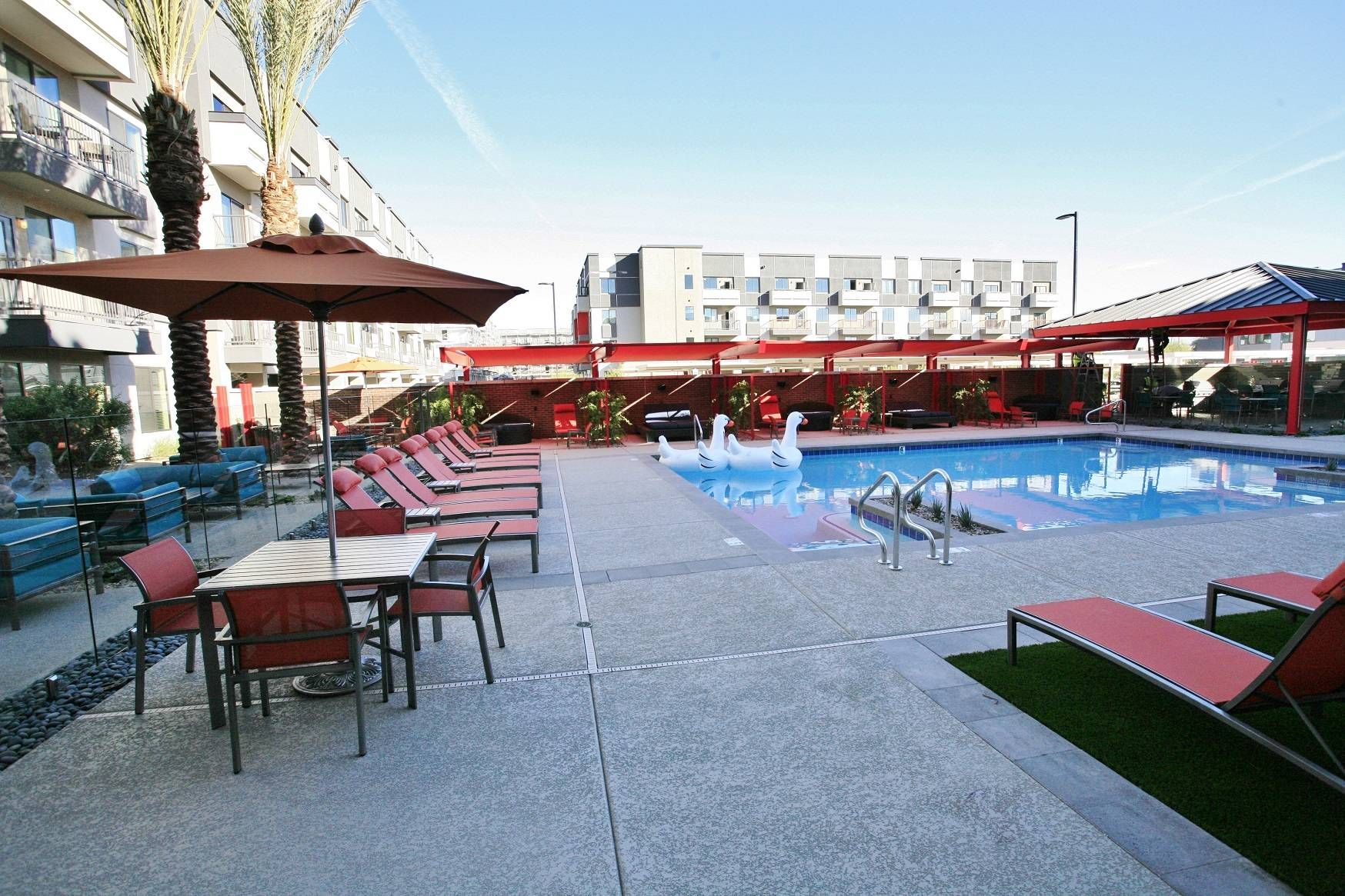 The pool area at Alta Steelyard Lofts, showcasing red sun loungers, palm trees, and a clear blue swimming pool.
