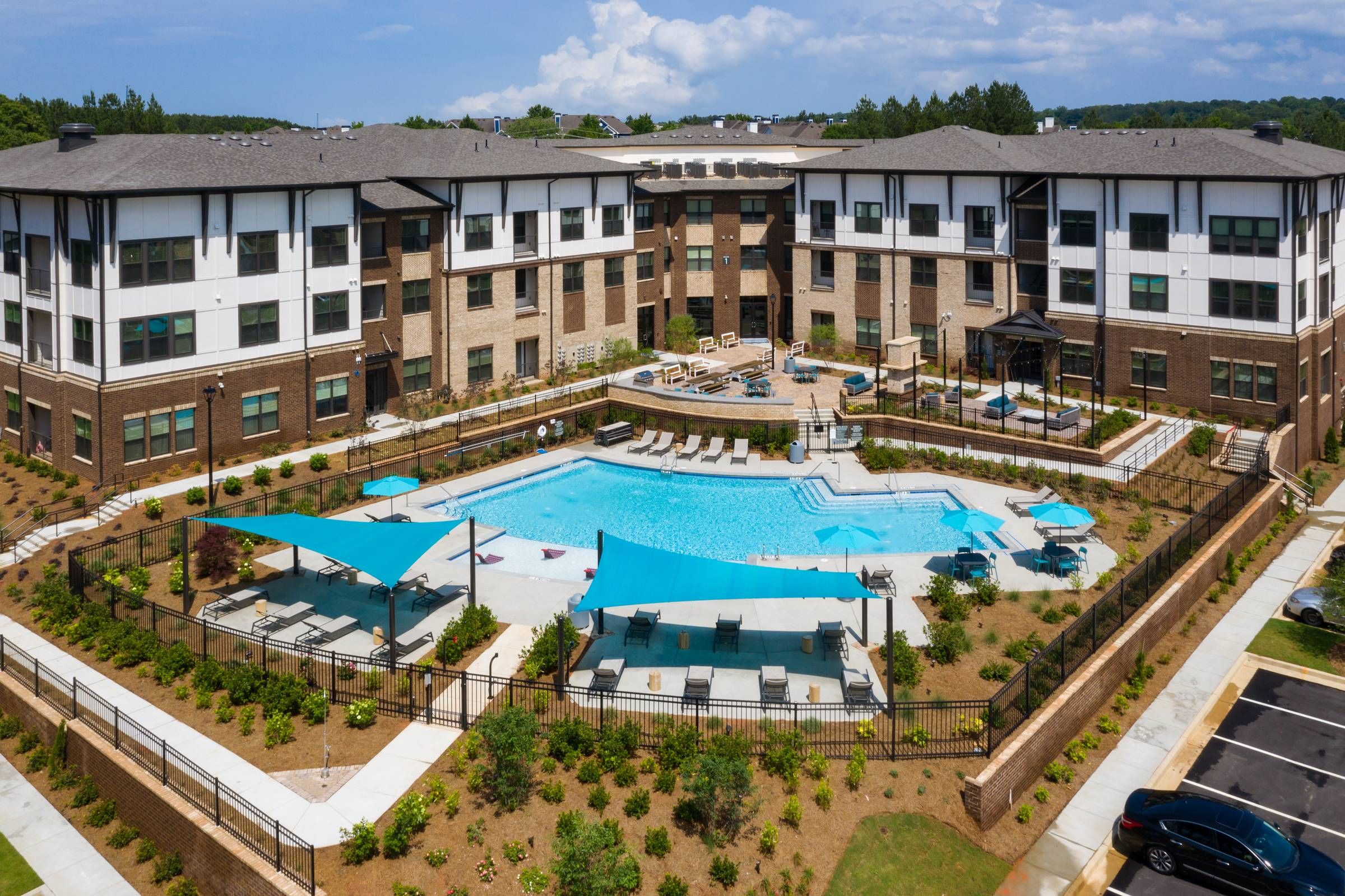 Aerial view of the Alta Sugarloaf apartment complex showcasing a large, L-shaped swimming pool with sun loungers and shade umbrellas.