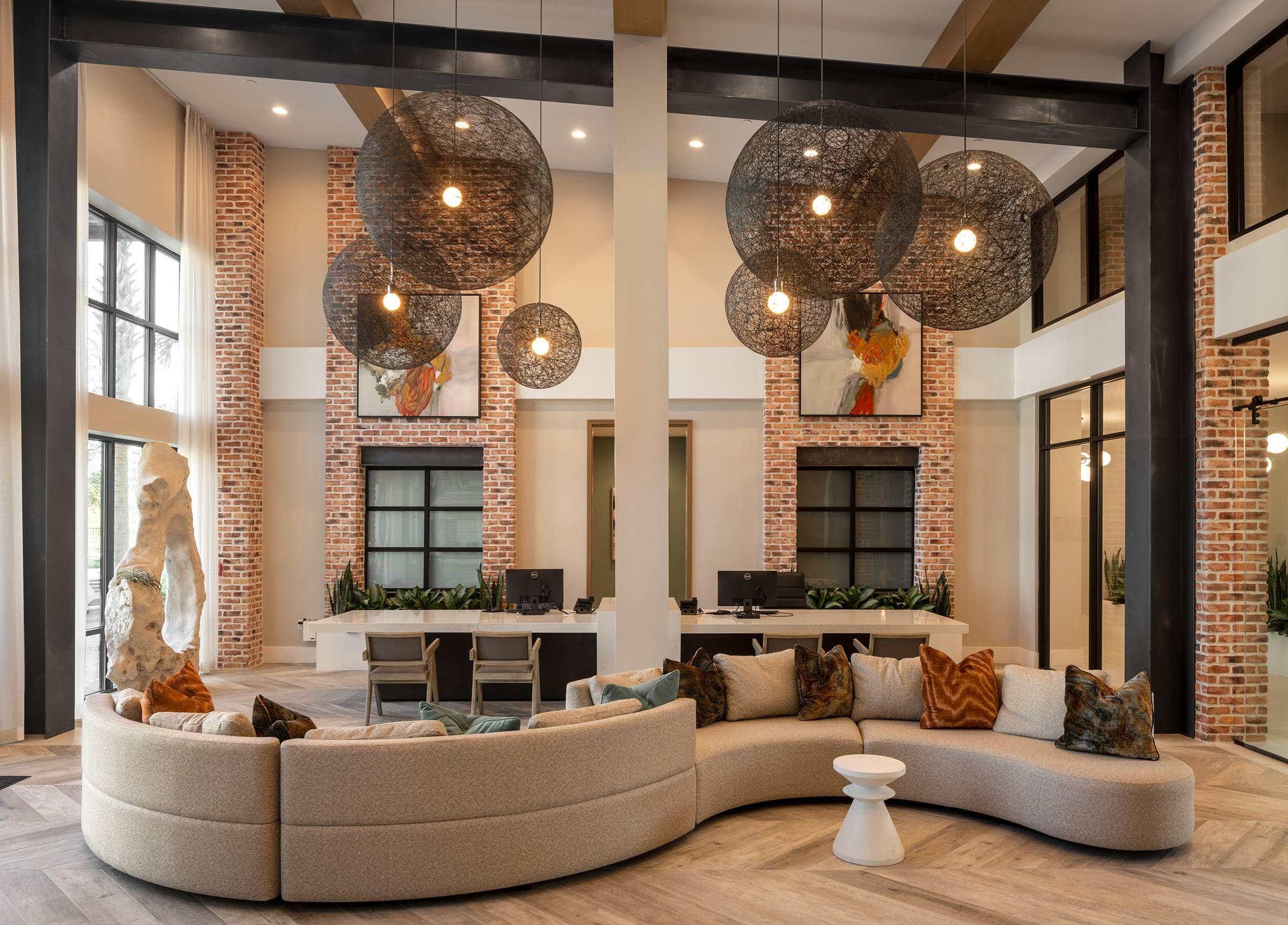 The lobby of Alta Winter Garden features a curvilinear sofa and spherical chandeliers, set against a backdrop of exposed brick and chic decor.