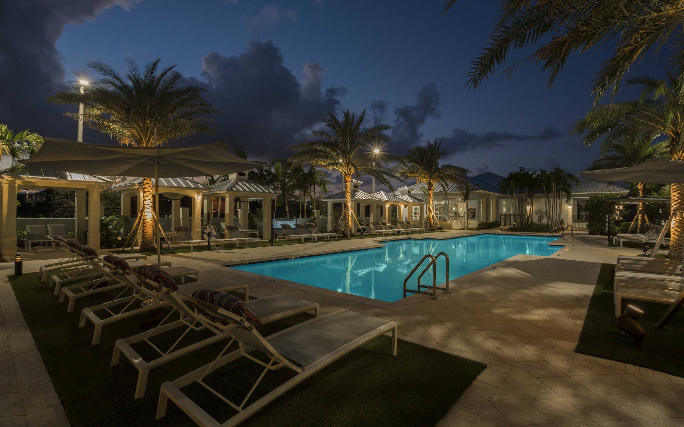 Delray Station pool area at night with bright blue water and lounge chairs.