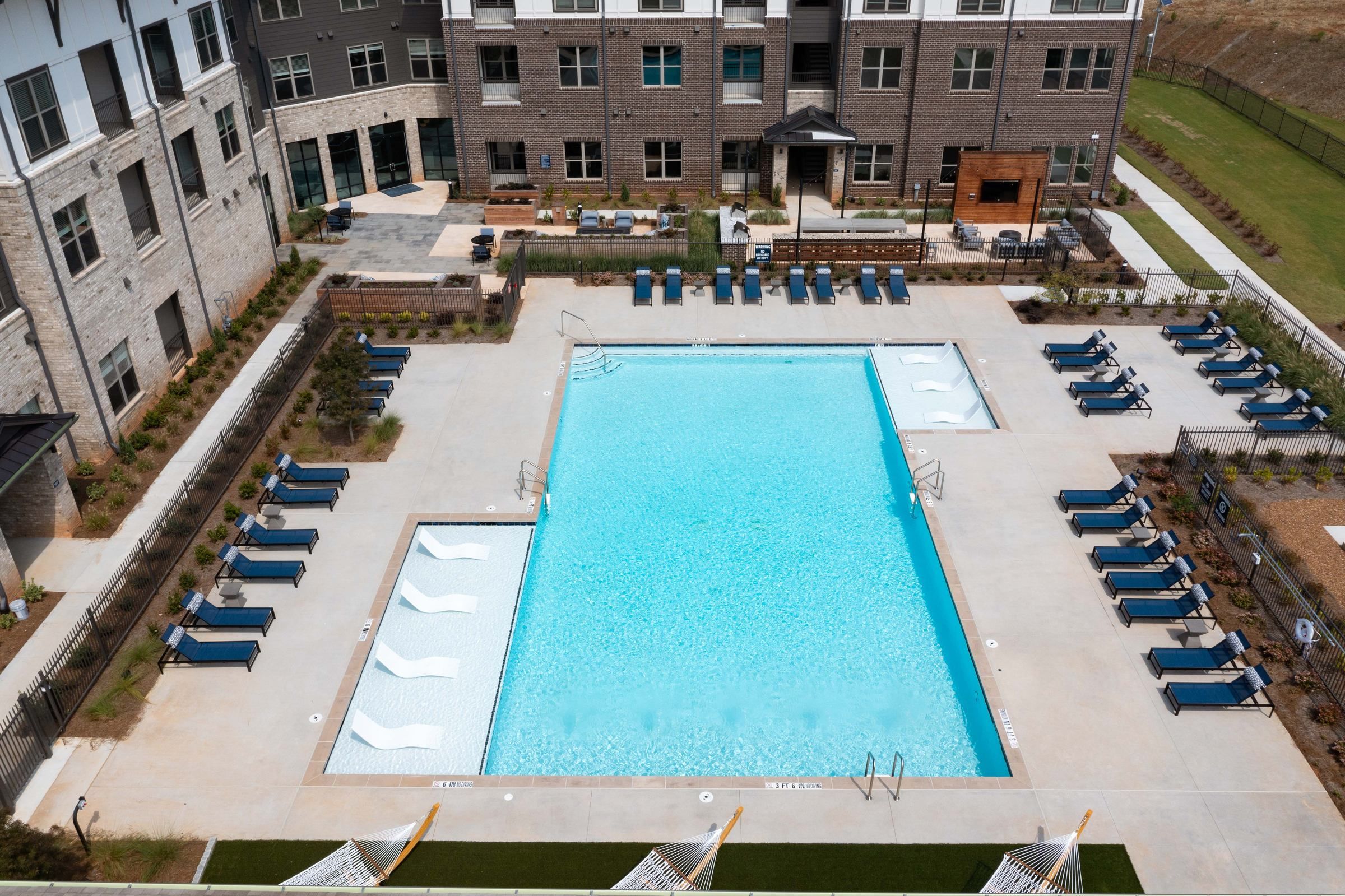 The outdoor pool of Alta Ashley Park as seen from above, featuring sparkling turquoise waters, white in-pool loungers, and neatly lined up sunbeds along the sides.
