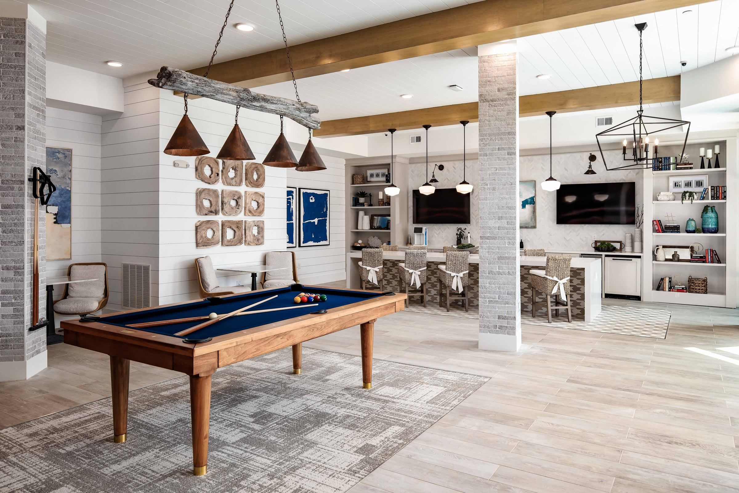 Alta Ashley Park's recreational room featuring a pool table with a rustic wood finish, pendant lighting, and cozy seating areas with shelves filled with books and decorative items.
