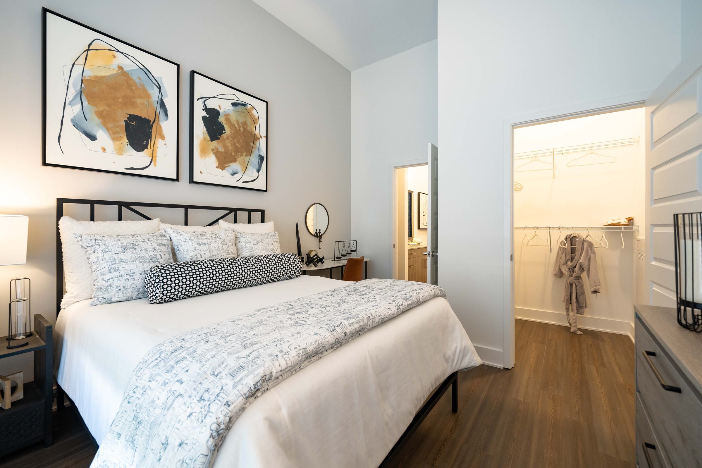 A comfortable bedroom at Alta Ashley Park, adorned with abstract art above the bed and a minimalistic design leading to a walk-in closet.