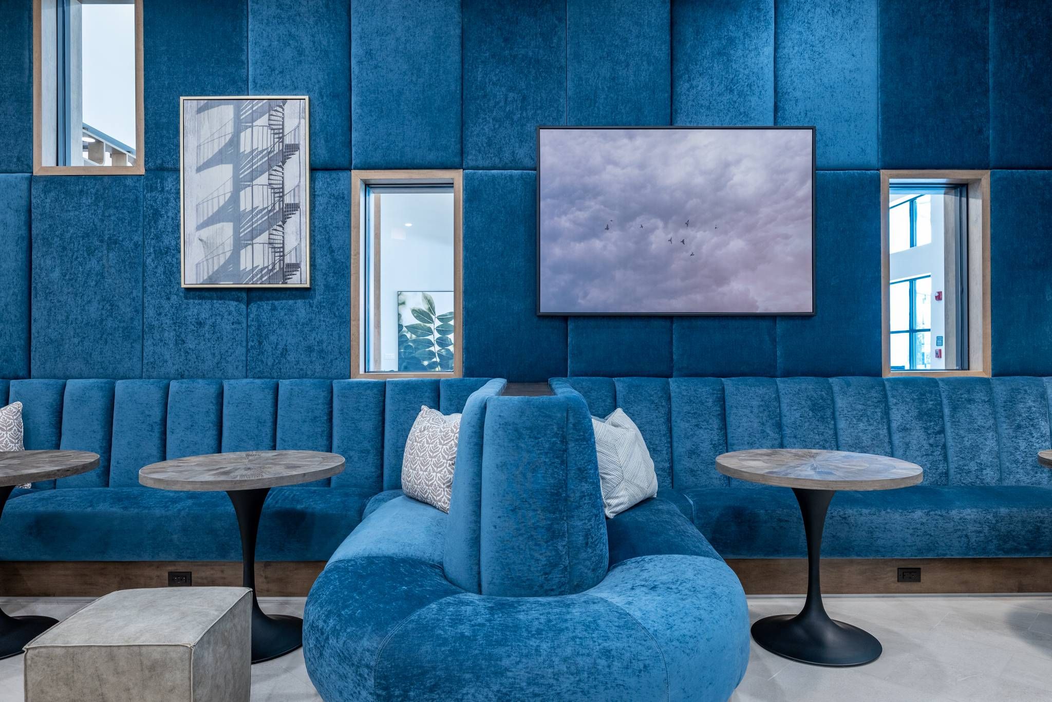 A cozy lounge area with plush blue sofas, stone-top tables, and vibrant wall art at Alta at Horizon West.