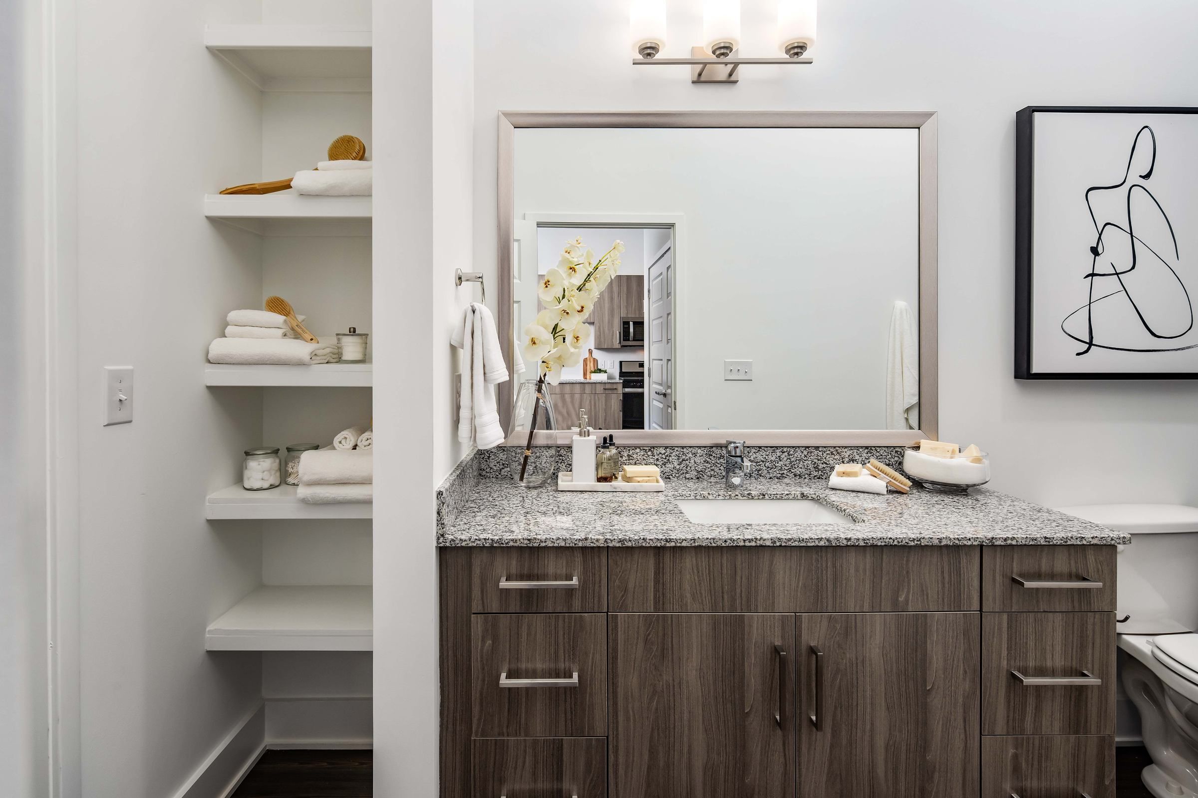 An inviting bathroom within Alta Ashley Park, with well-organized shelves, a spacious vanity area, and soft lighting that creates a warm ambiance.