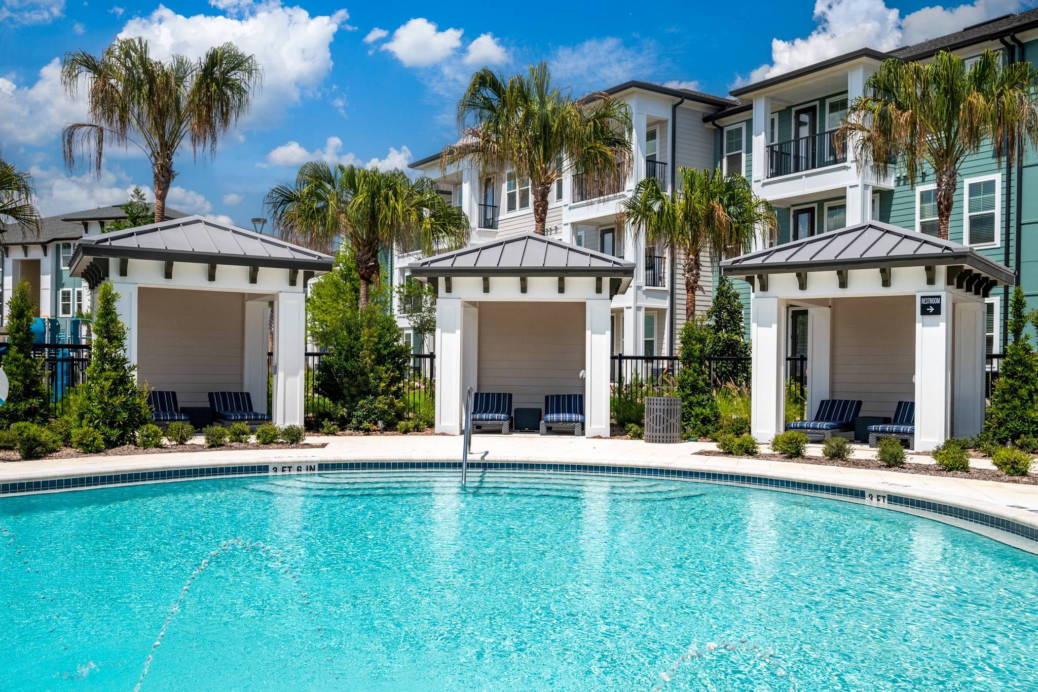 Poolside cabanas with blue striped cushions and a serene swimming pool reflect the sunny, tropical ambiance of Alta at Horizon West.