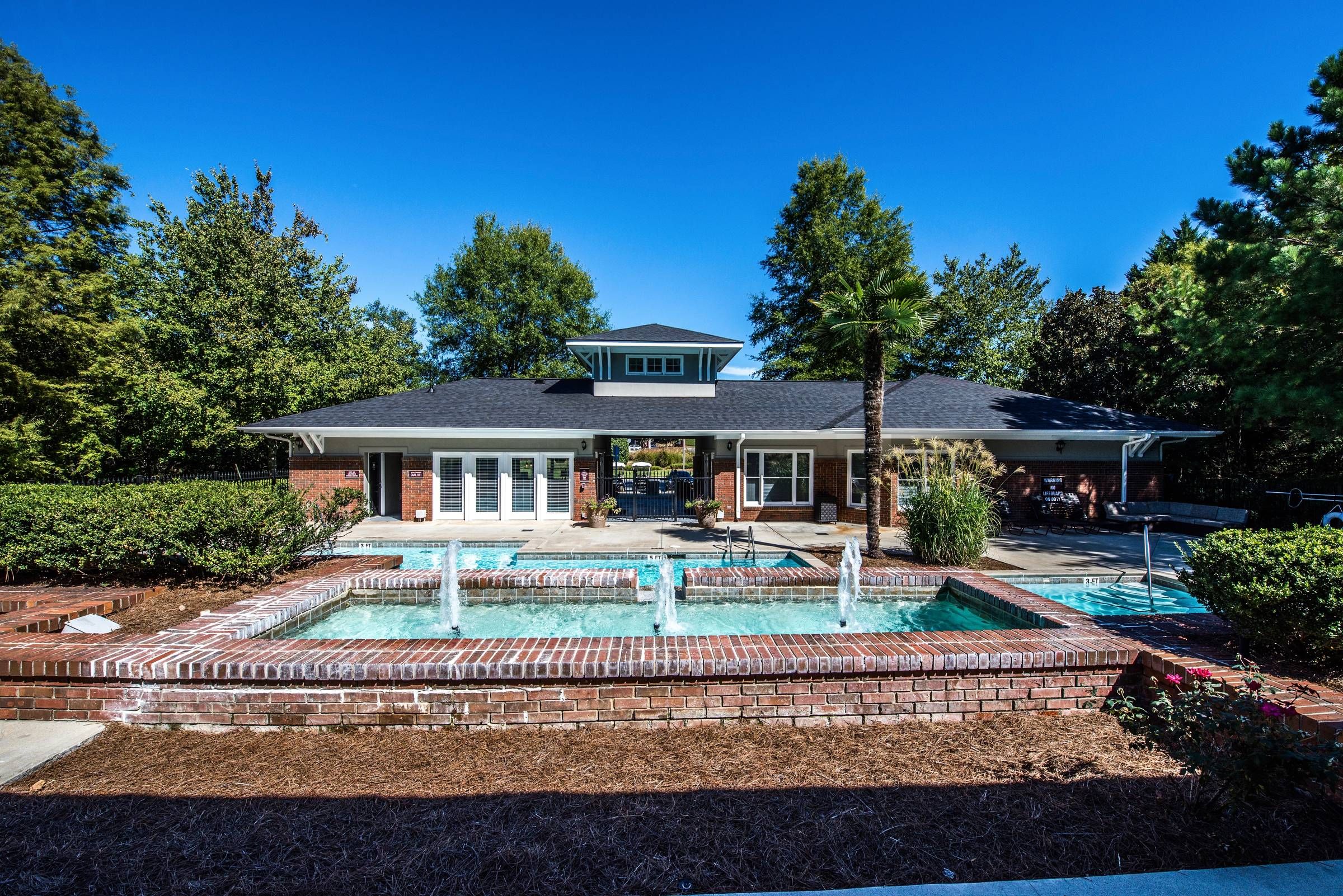 Altera Riverside exterior view of clubhouse with pool and water fountain feature.