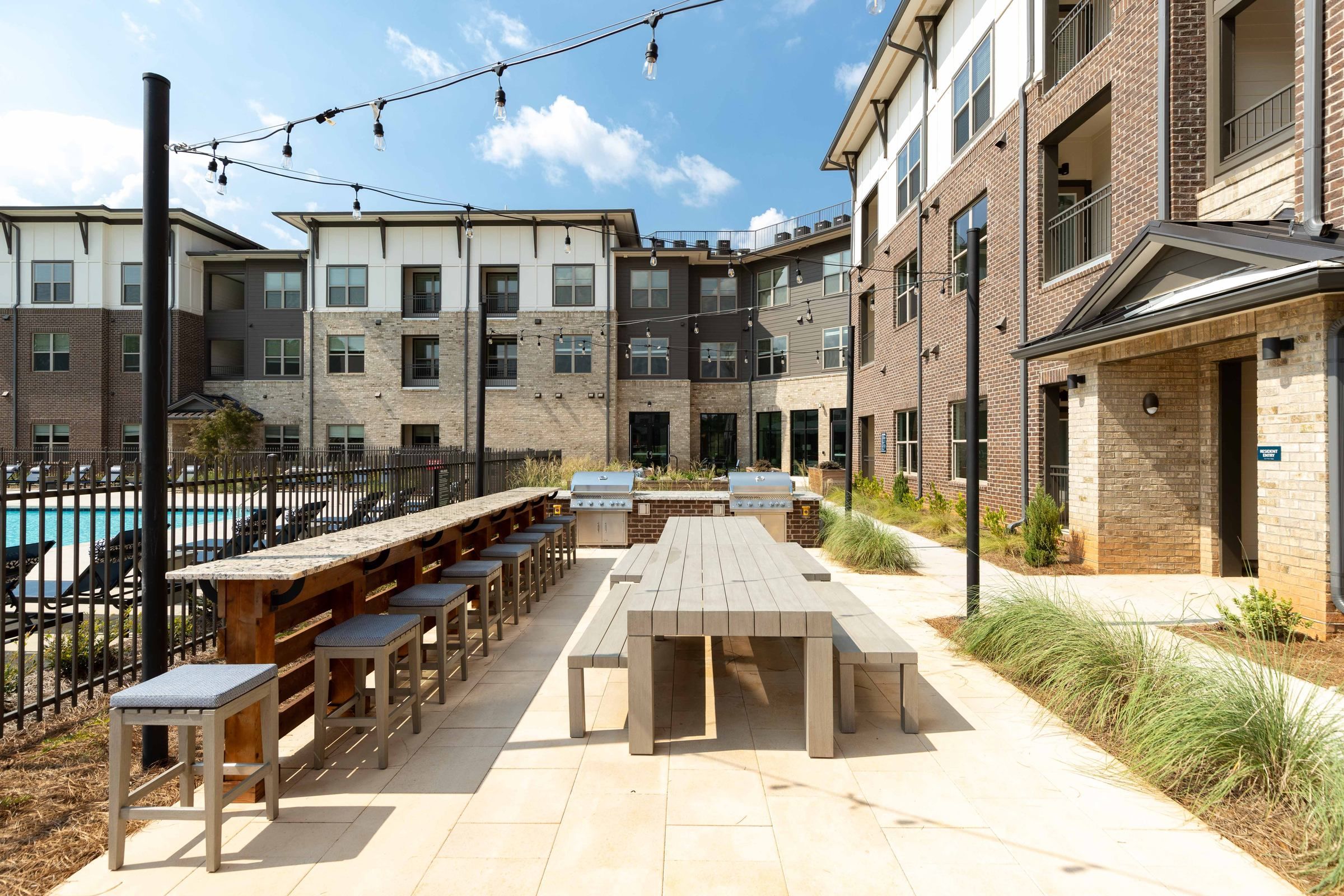 The outdoor communal dining and barbecue area at Alta Ashley Park, complete with long picnic tables and grills, inviting residents to enjoy alfresco gatherings.
