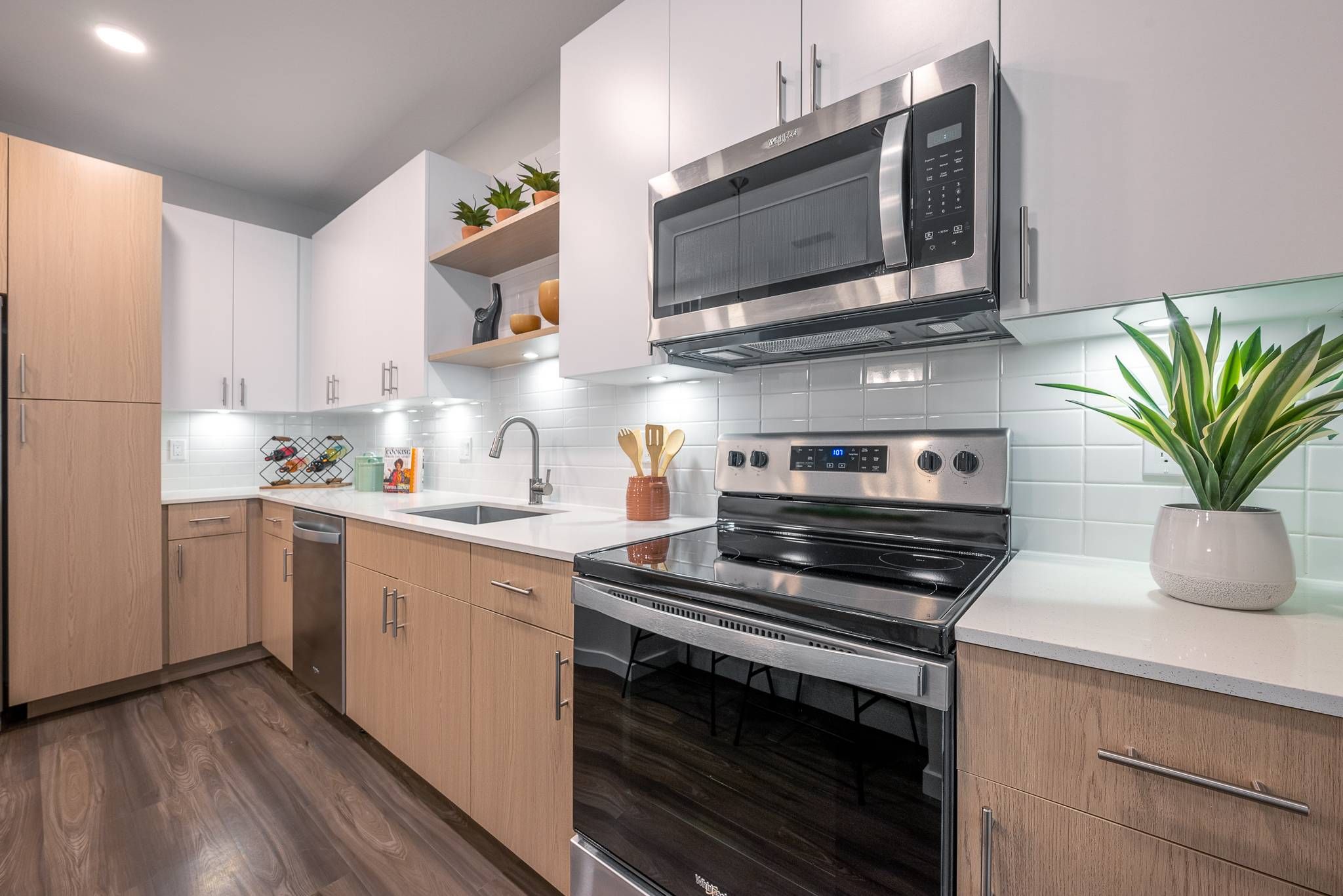 A tidy one-bedroom apartment kitchen in Alta at Horizon West featuring modern appliances and white cabinetry with wood accents.