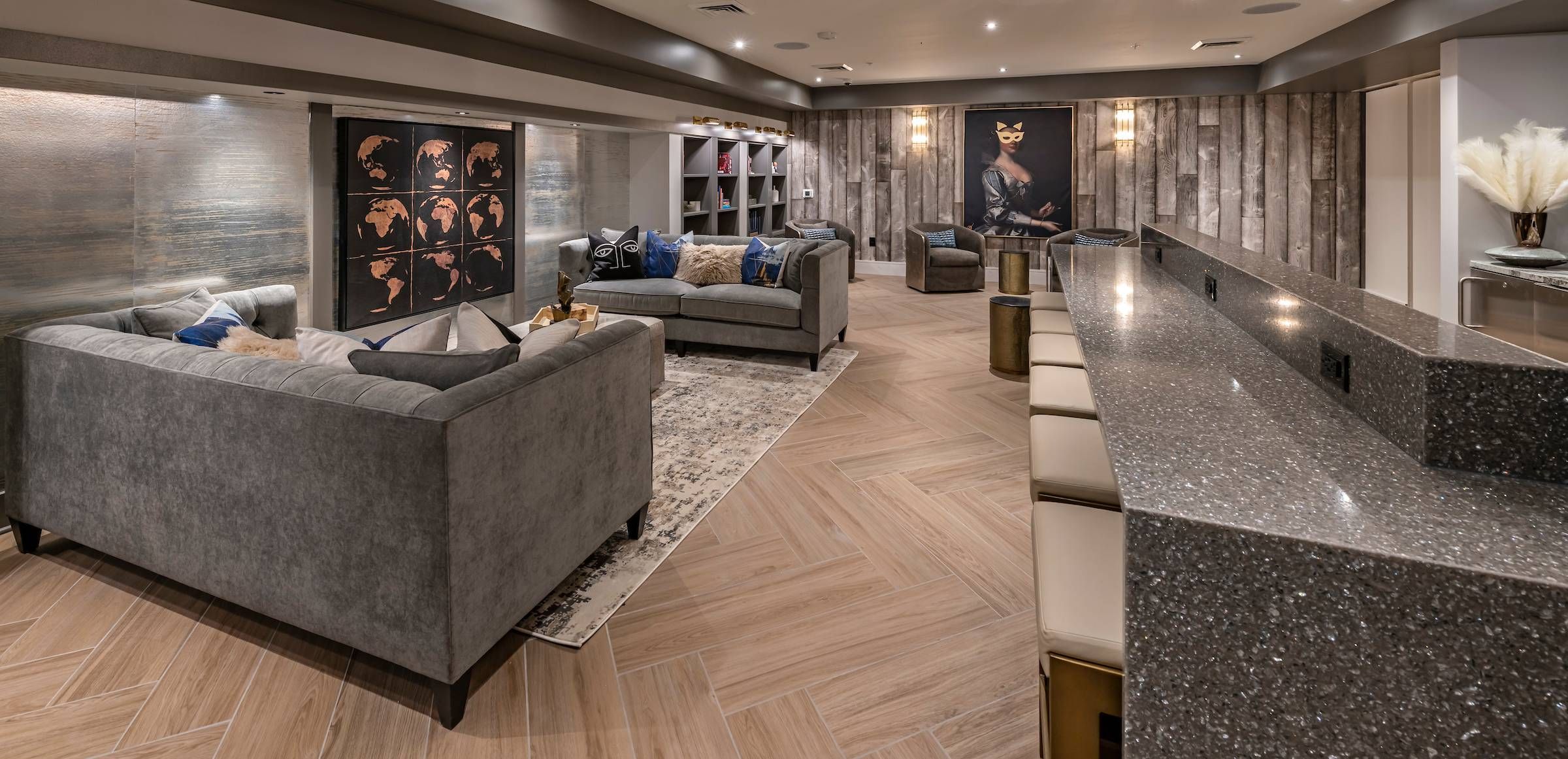 Alta Southern Highlands presents a chic clubhouse lounge area with plush grey sofas, a sparkling kitchen counter, and artistic wall decor.