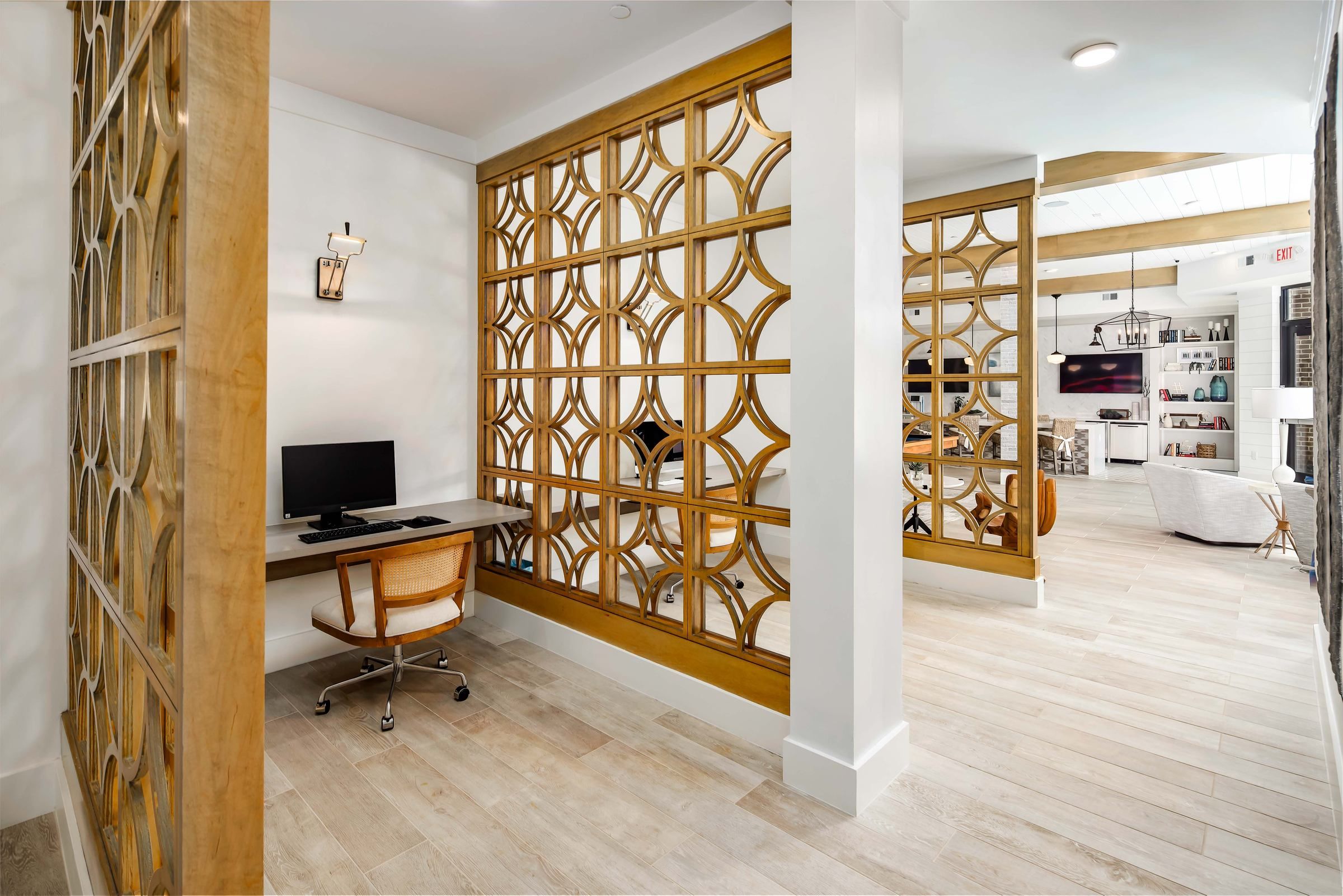 A modern office space within Alta Ashley Park, bordered by ornate wooden partitioning, showcasing a neat desk with a computer and a woven office chair.