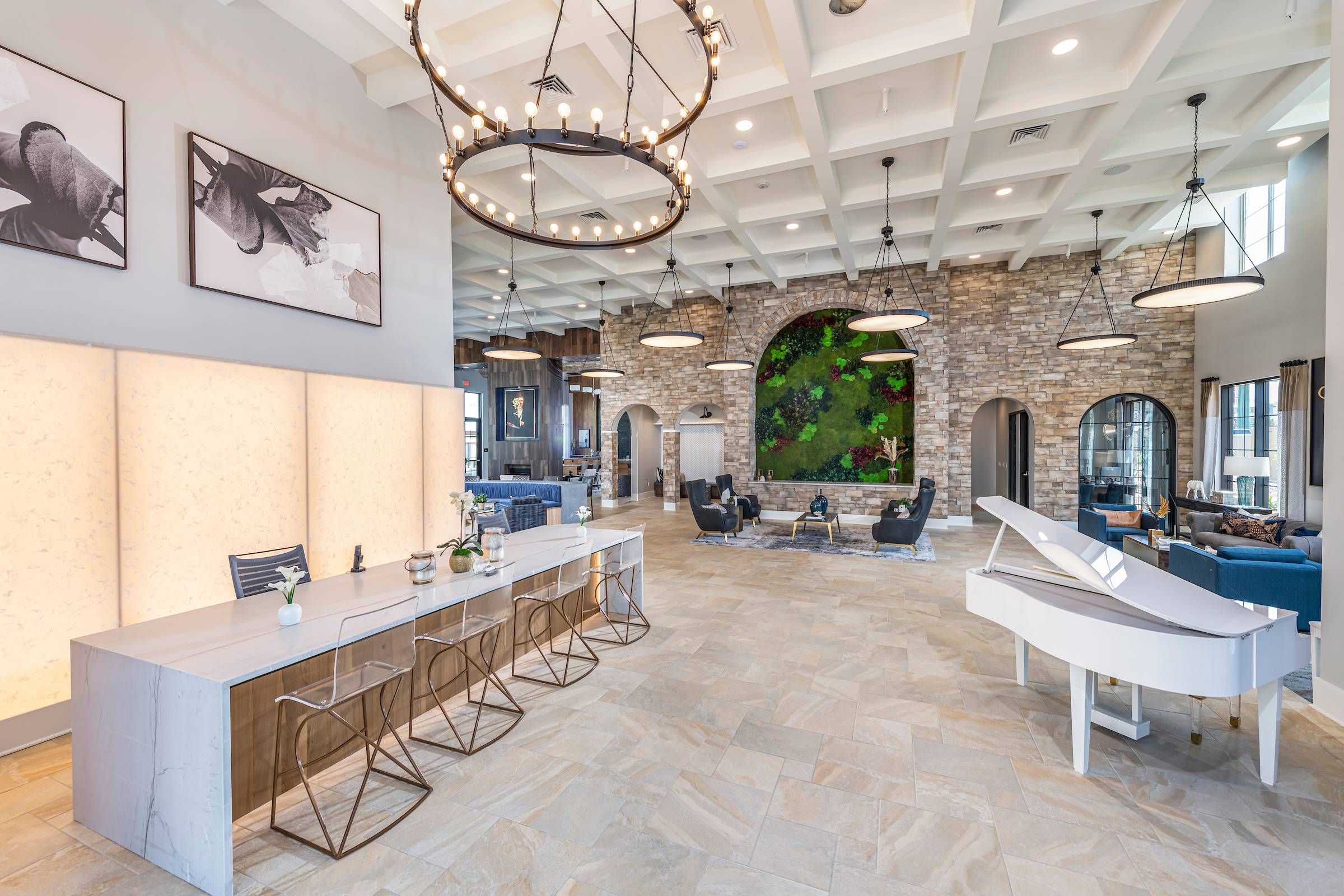 The grand lobby of Alta Southern Highlands showcases a white piano, circular chandelier, and a cozy seating arrangement.