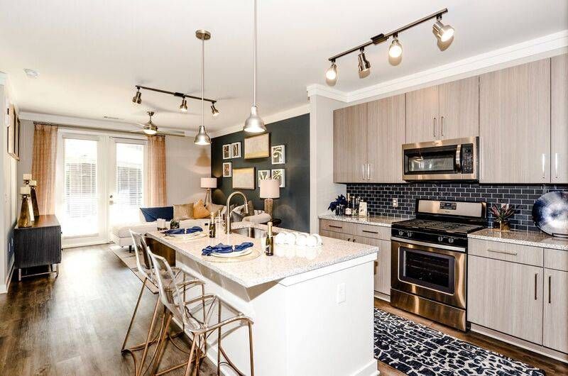 A chic kitchen with modern bar stools, stainless steel appliances, and a mosaic tile backsplash in a model apartment at Alta at Jonquil.