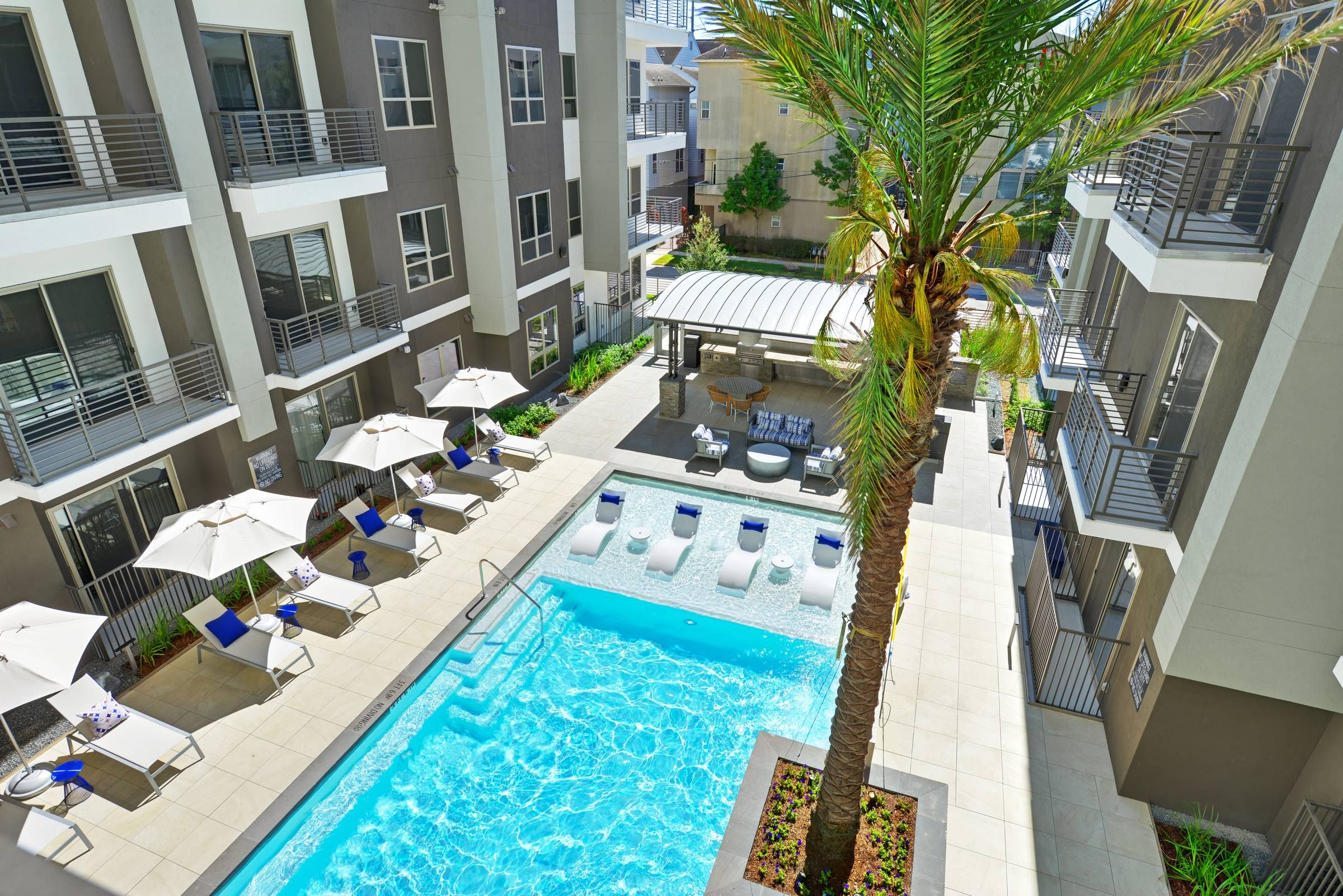 A well-appointed living room at Alta West Gray opens to a pool view, highlighted by a blue sectional sofa and chic interior design.