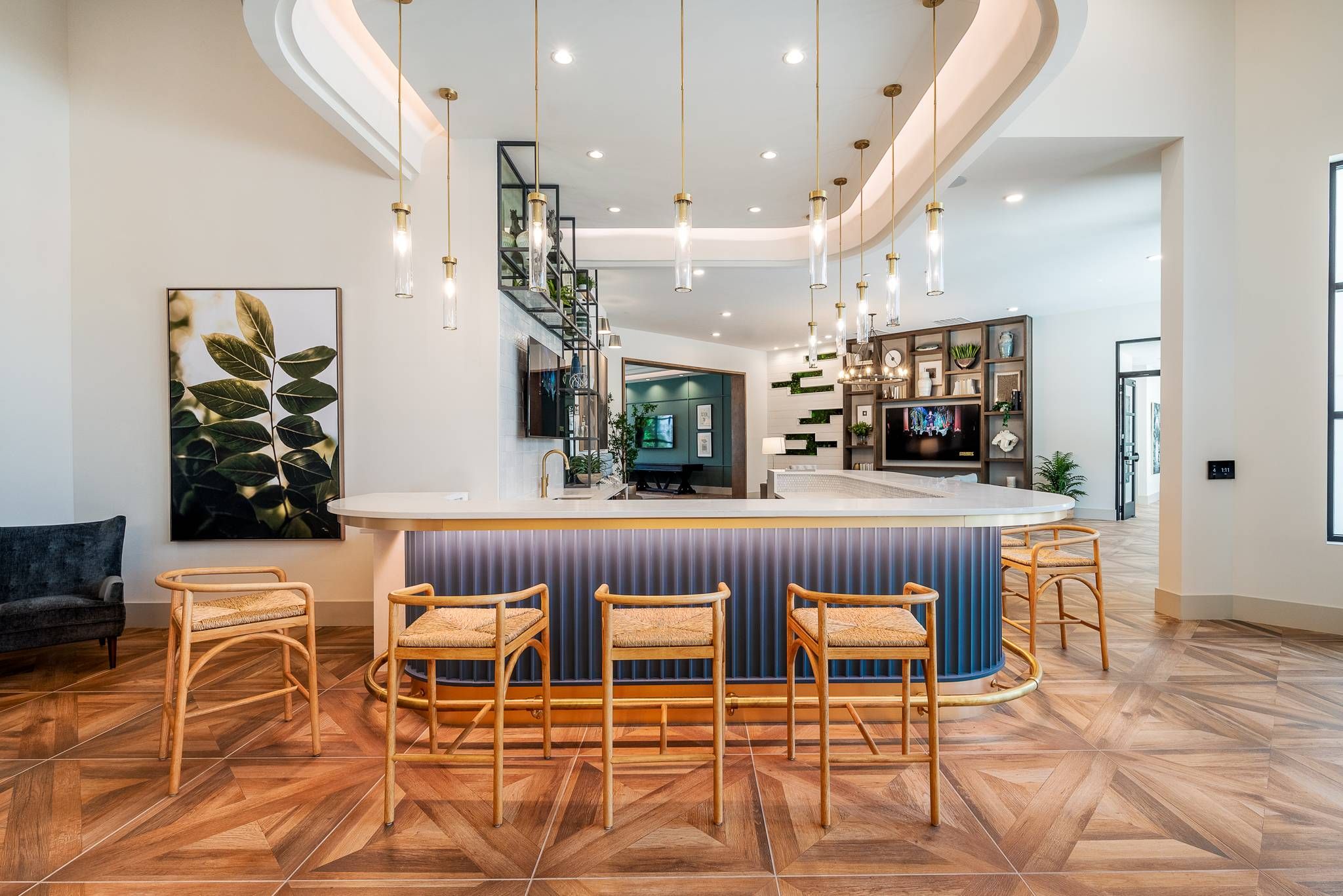 A modern kitchen bar area with herringbone wood flooring, three rattan bar stools, and elegant pendant lights in Alta at Horizon West's communal space.