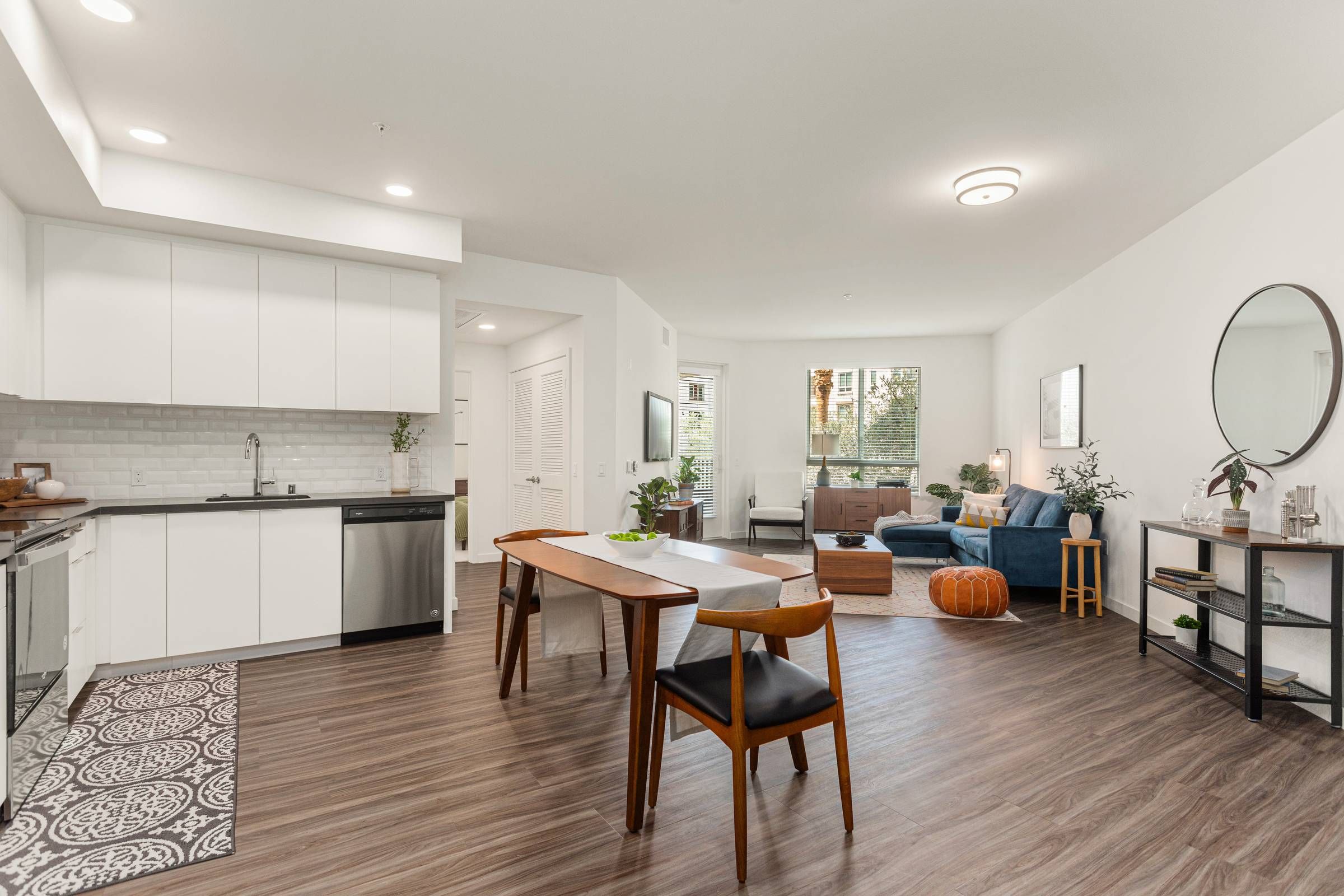 Inside an Alta Upland apartment, an open plan design combines a sleek, modern kitchen with a dining area and a comfortable living space accented with vibrant blue furniture.