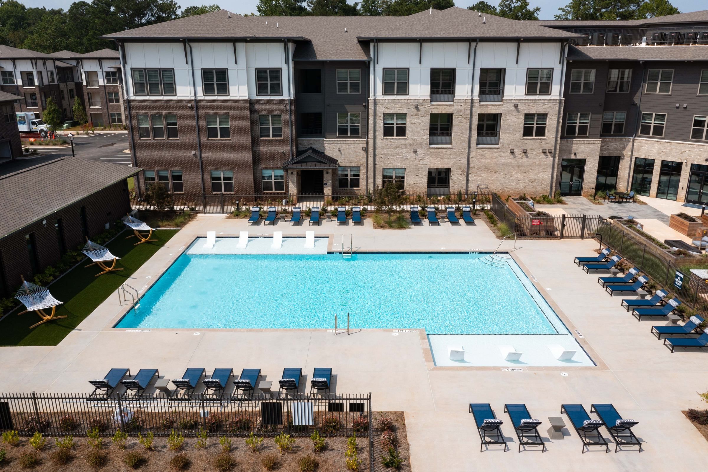 Overhead view of the vibrant blue swimming pool at Alta Ashley Park, surrounded by lounge chairs and sun umbrellas, nestled within the apartment complex.