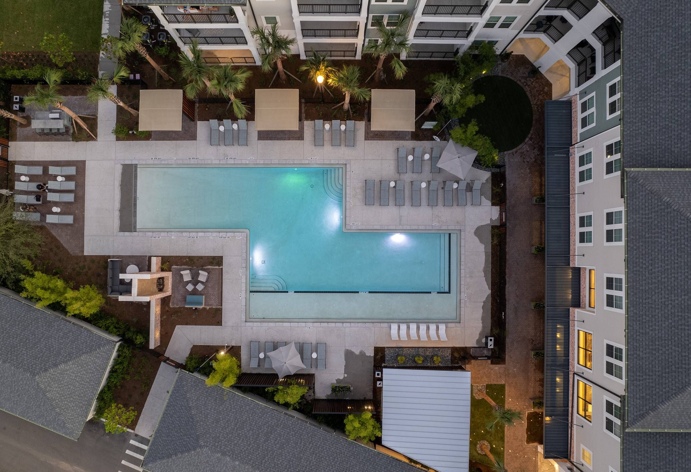 Evening aerial view of Alta Winter Garden's pool deck with glowing lights, showcasing a tranquil pool surrounded by loungers and palm trees.