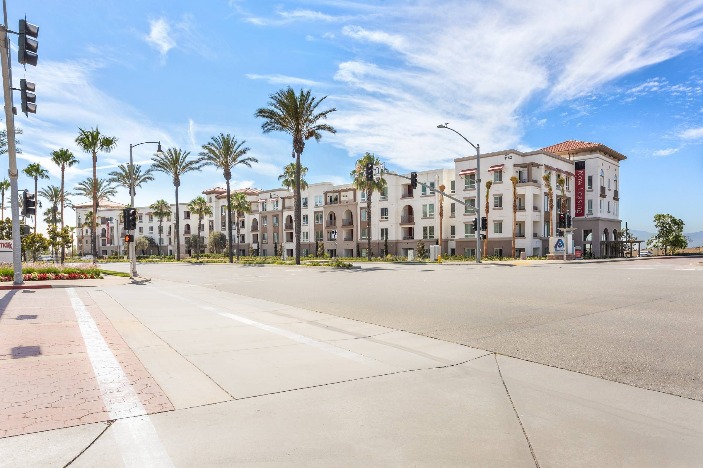 A grand exterior view of Alta Upland showcasing its Mediterranean-inspired architecture, flanked by palm trees under a blue sky.
