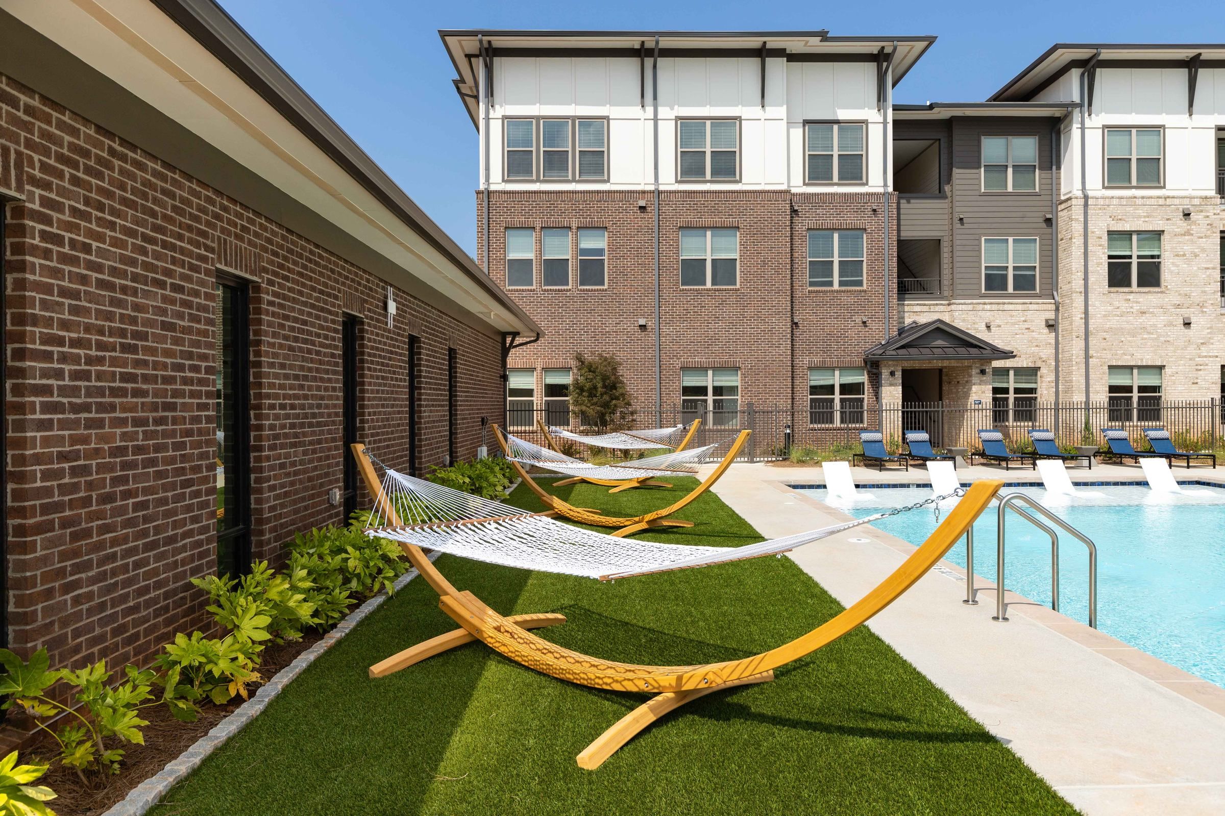 Tranquil poolside ambiance at Alta Ashley Park with hammocks on artificial grass, offering a relaxing outdoor retreat adjacent to the apartment buildings.