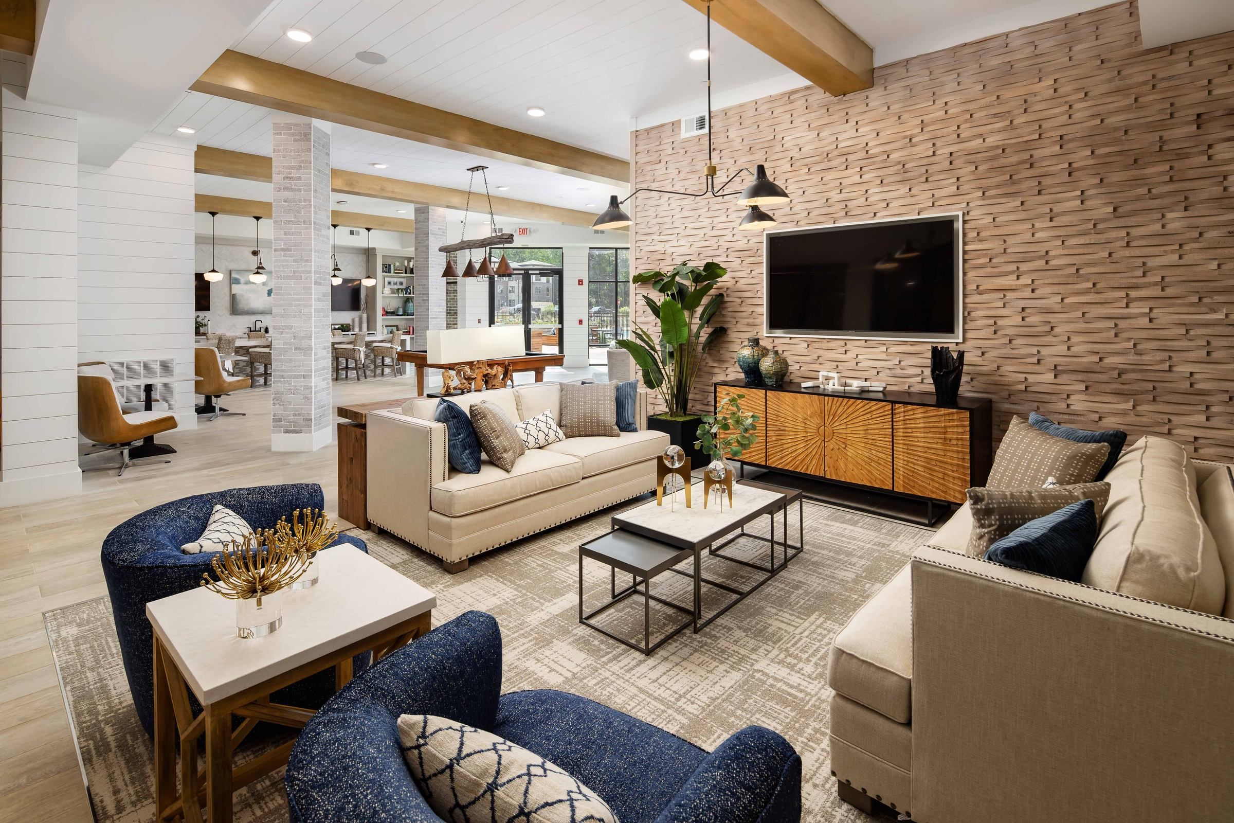 The open-plan living space at Alta Ashley Park, highlighting a plush cream sofa, a blue armchair, and a contemporary black coffee table over a textured rug, with a view into the bedroom.