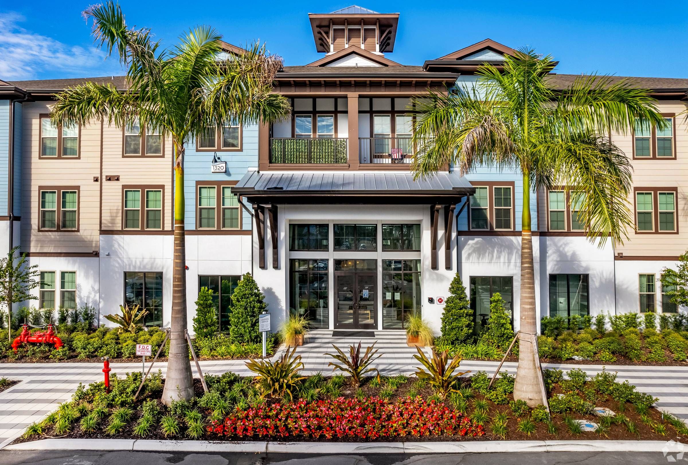 The front entrance of the Alta Sugarloaf apartment complex, showcasing a well-manicured landscape with tropical plants and a welcoming pathway.