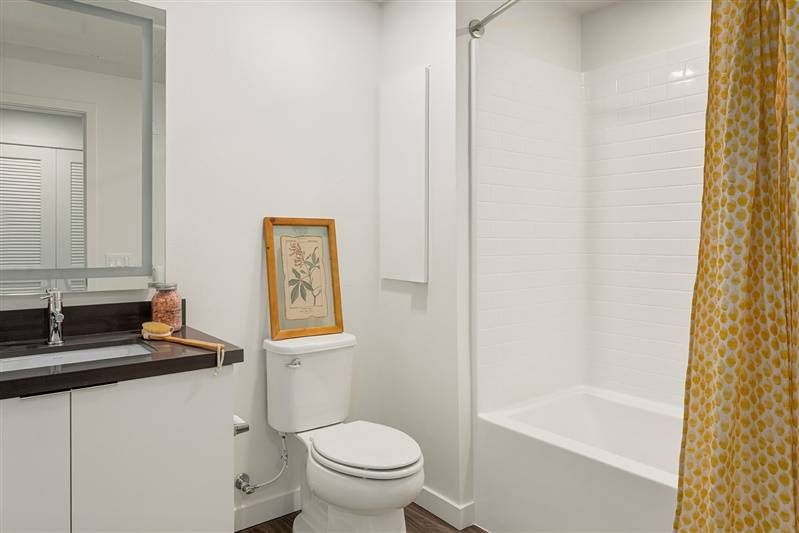 Alta Upland’s bathroom is a blend of modernity and warmth, with a wooden vanity, a framed botanical print, and a shower with a patterned yellow curtain.