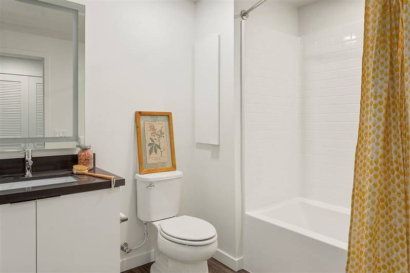 Alta Upland’s bathroom is a blend of modernity and warmth, with a wooden vanity, a framed botanical print, and a shower with a patterned yellow curtain.