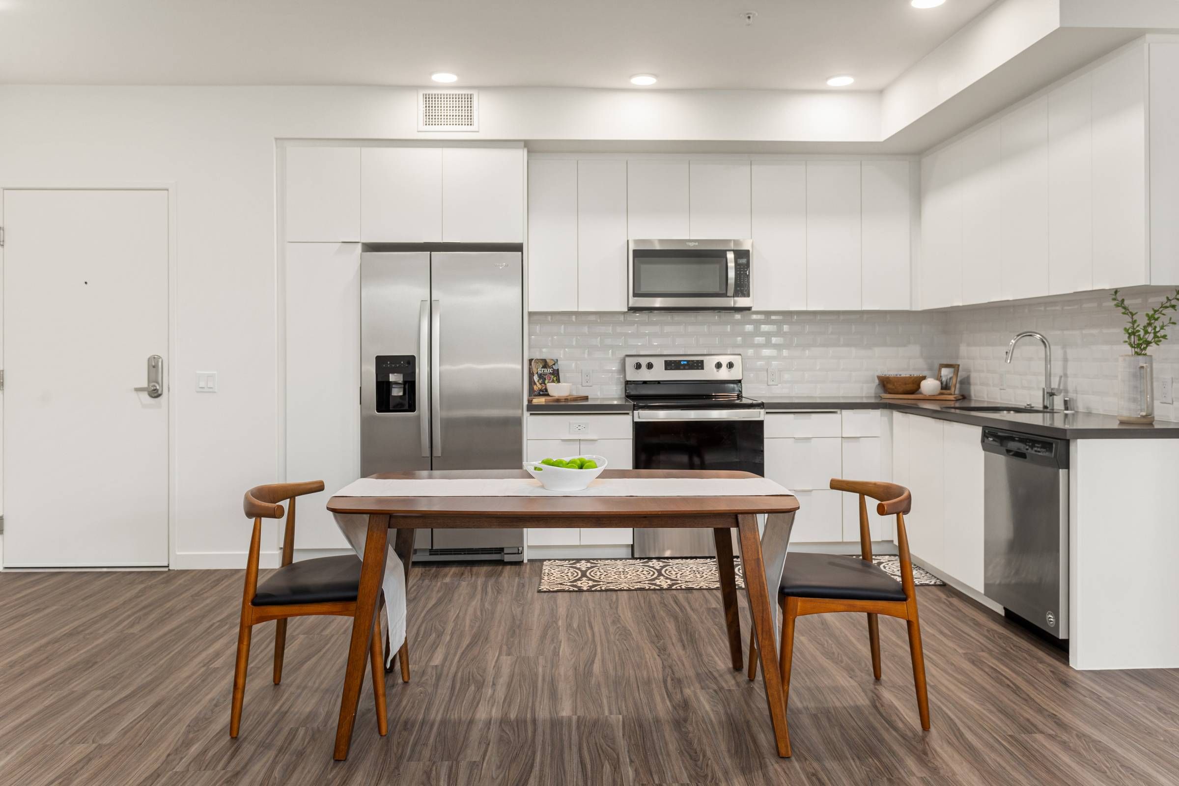 An inviting Alta Upland kitchen with white cabinetry and subway tile backsplash, featuring a wooden dining table and mid-century modern chairs.