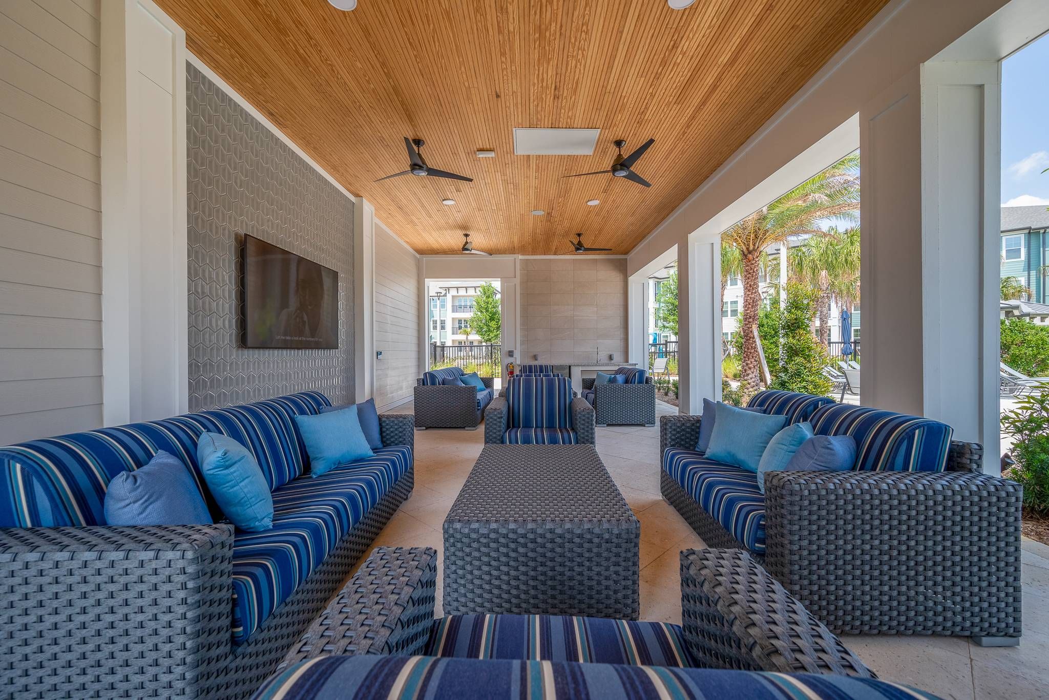 A spacious covered outdoor lounge featuring striped sofas and wicker furniture under a wood-paneled ceiling at Alta at Horizon West.