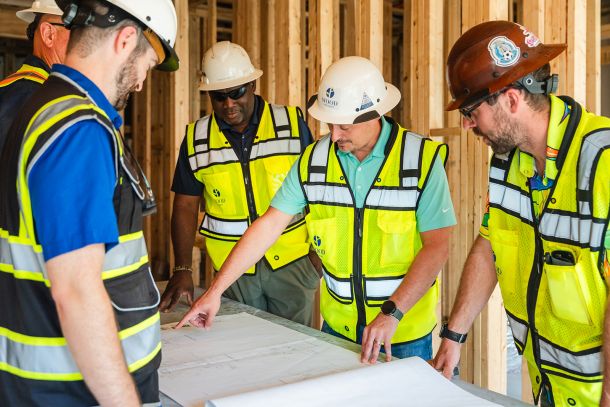 Group of construction workers look up a giant red crane structure