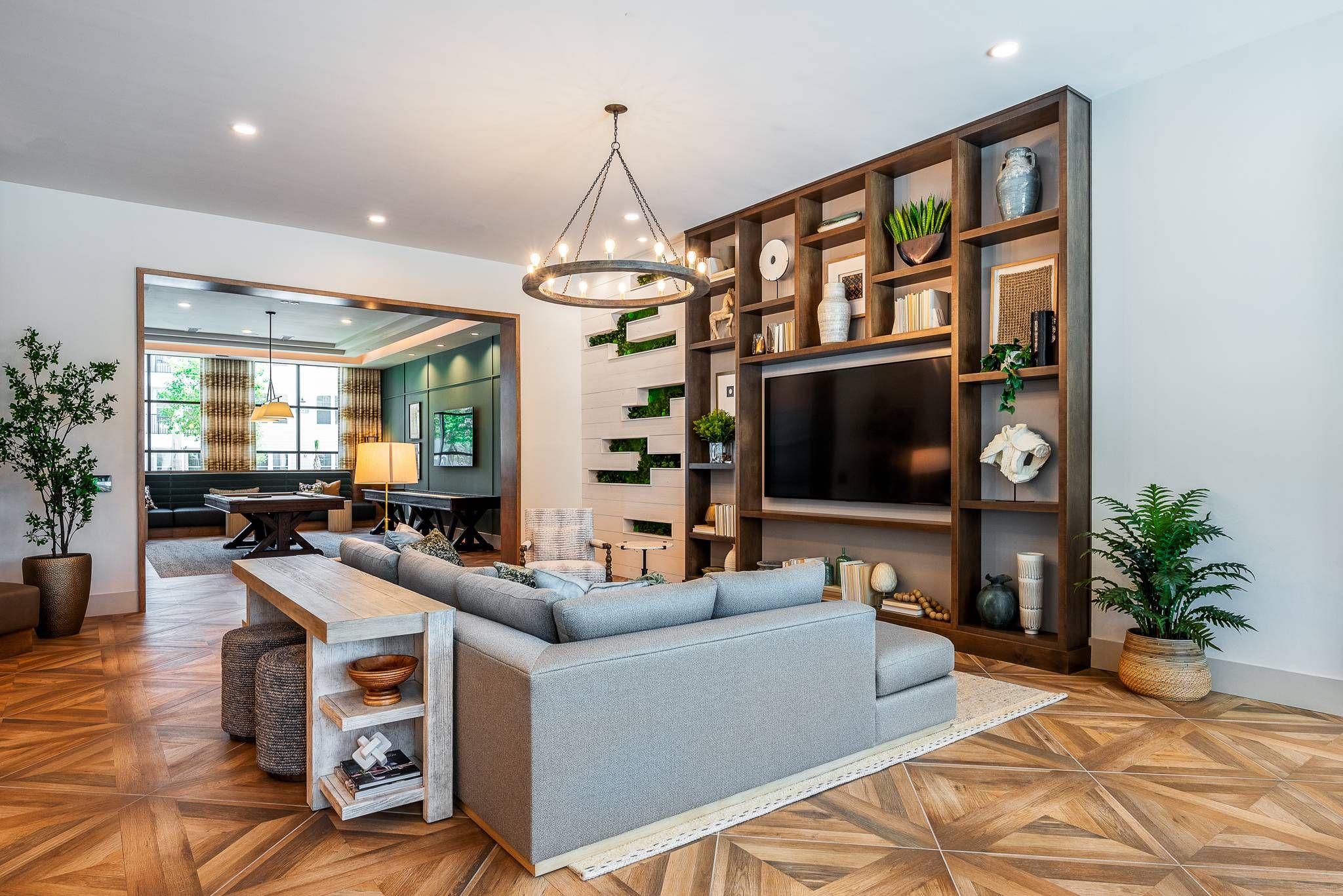 A stylish lounge area with a large gray sofa, wooden bookshelves, and a chic circular chandelier in the common area of Alta at Horizon West.