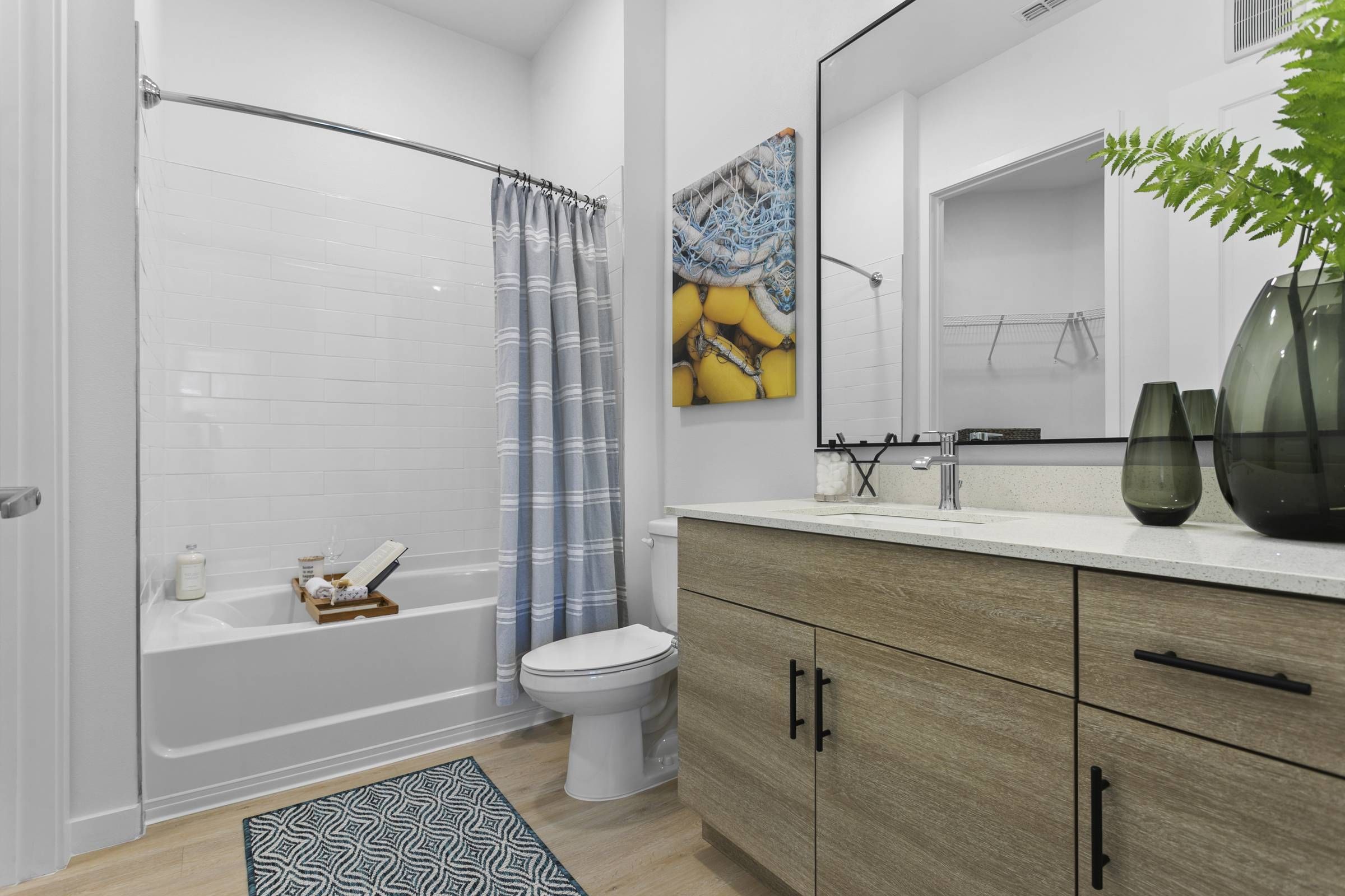 The Alta Clearwater bathroom features a spacious white-tiled shower, gray vanity with modern fixtures, and a colorful wall art of a yellow buoy.