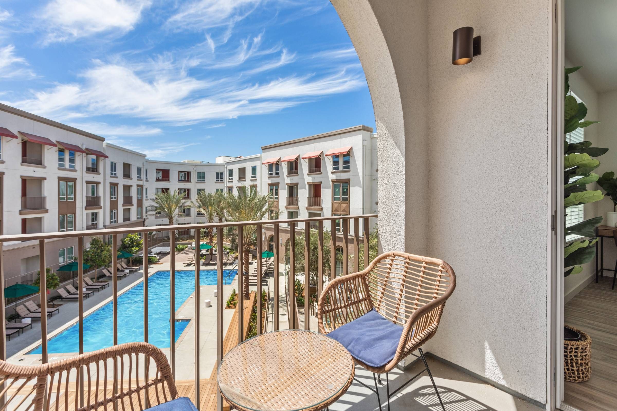 A view from the balcony at Alta Upland overlooking the resort-style pool area, with comfortable wicker chairs inviting relaxation.