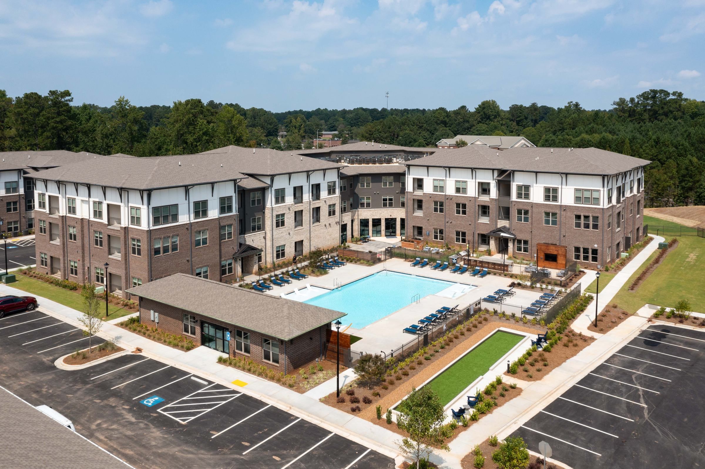 Aerial view of Alta Ashley Park showcasing the expansive outdoor pool area flanked by a large apartment building with a gray and brown brick facade.