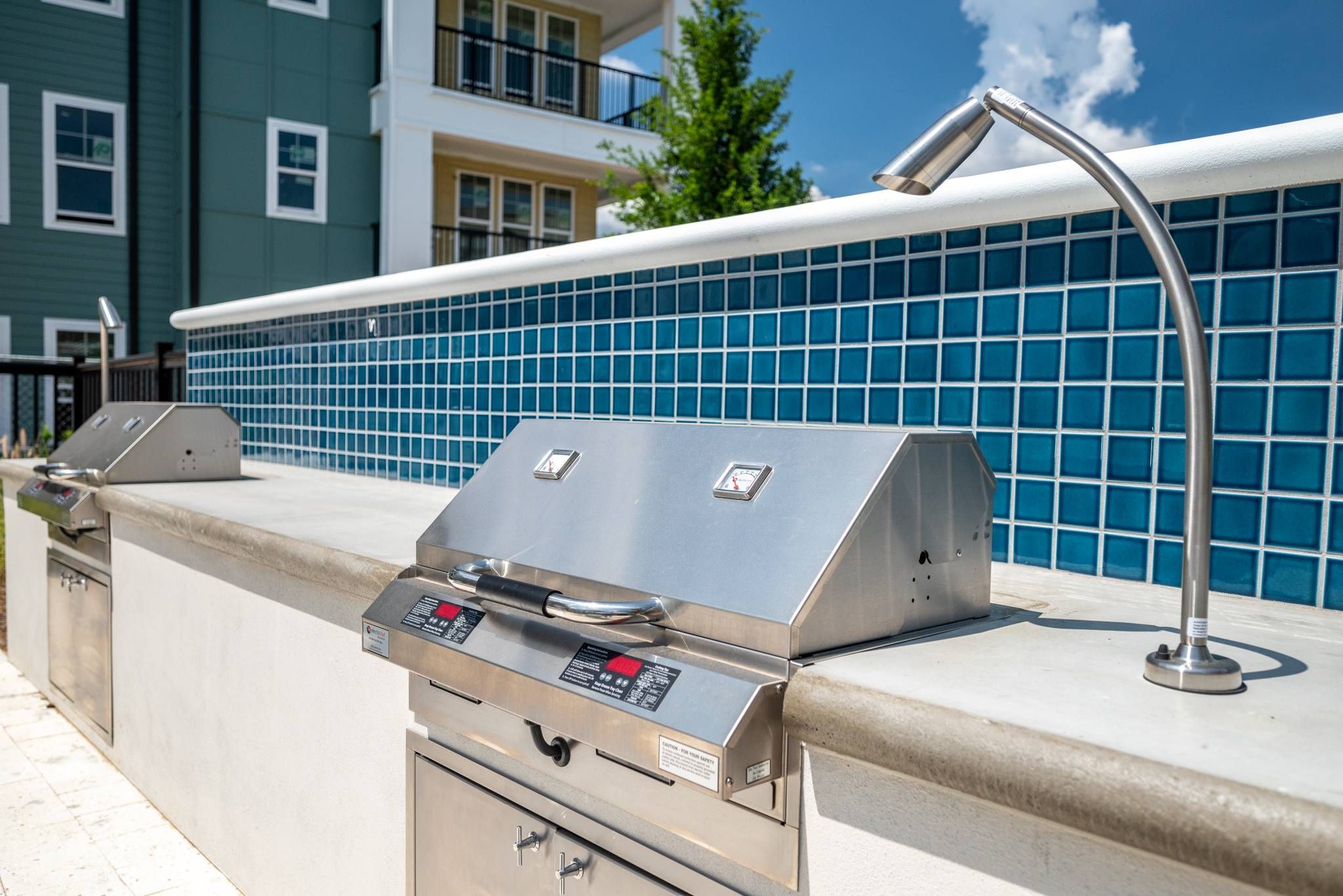 A modern outdoor grilling station with stainless steel appliances and blue tile backsplash set for resident cookouts at Alta at Horizon West.