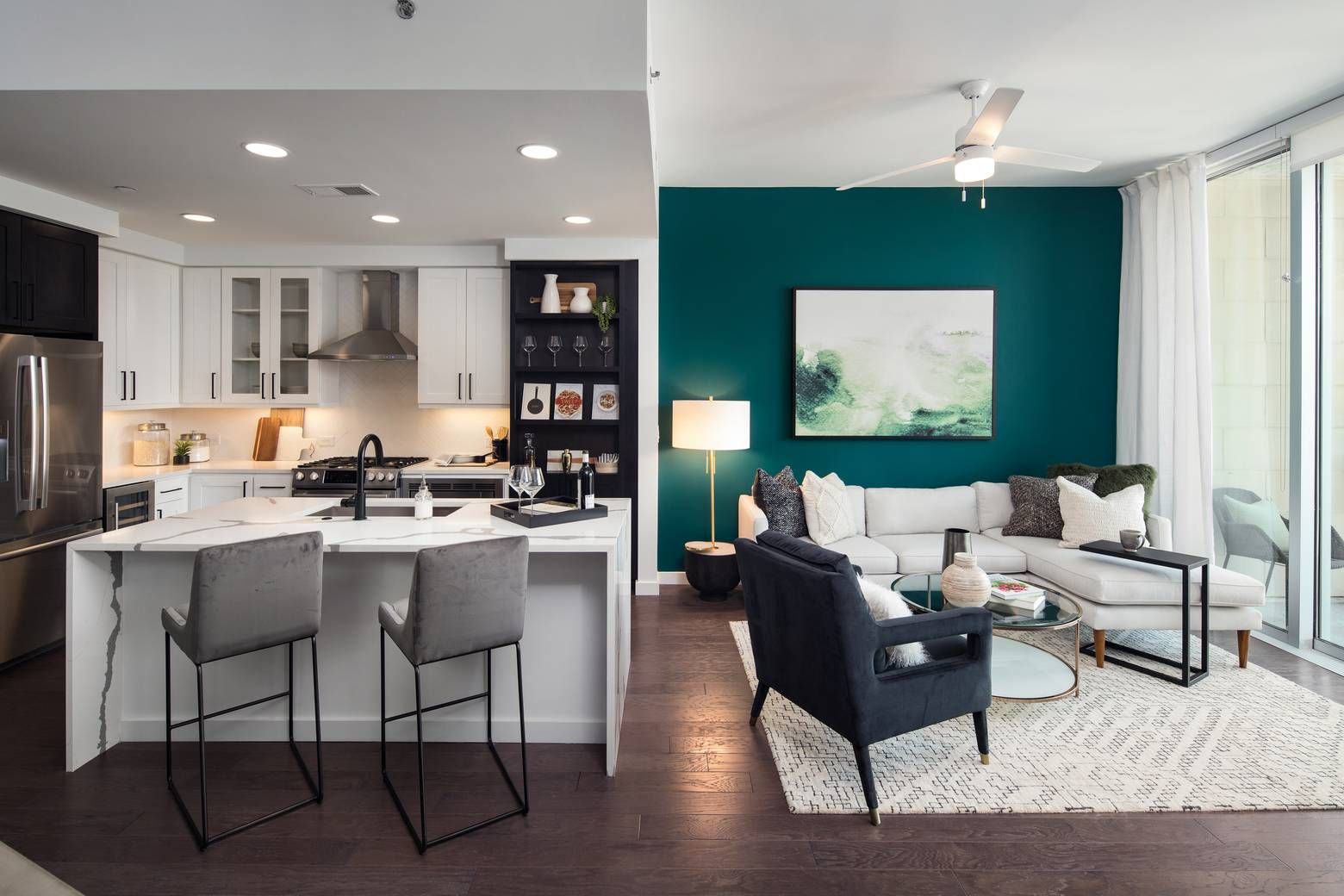 The Huntley open plan kitchen and living area with hardwood floors, large sliding glass door, and green accent wall.