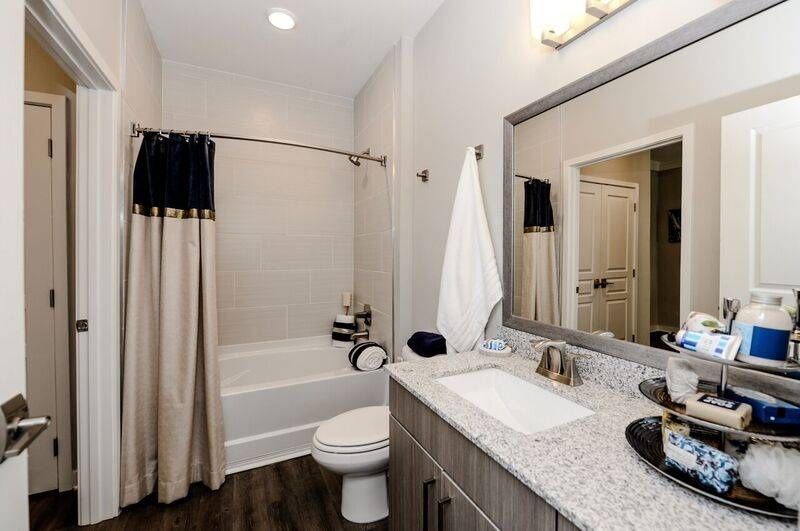 A modern bathroom in Alta at Jonquil featuring a rectangular undermount sink, granite countertops, and a shower-tub combo with a cream and navy shower curtain.