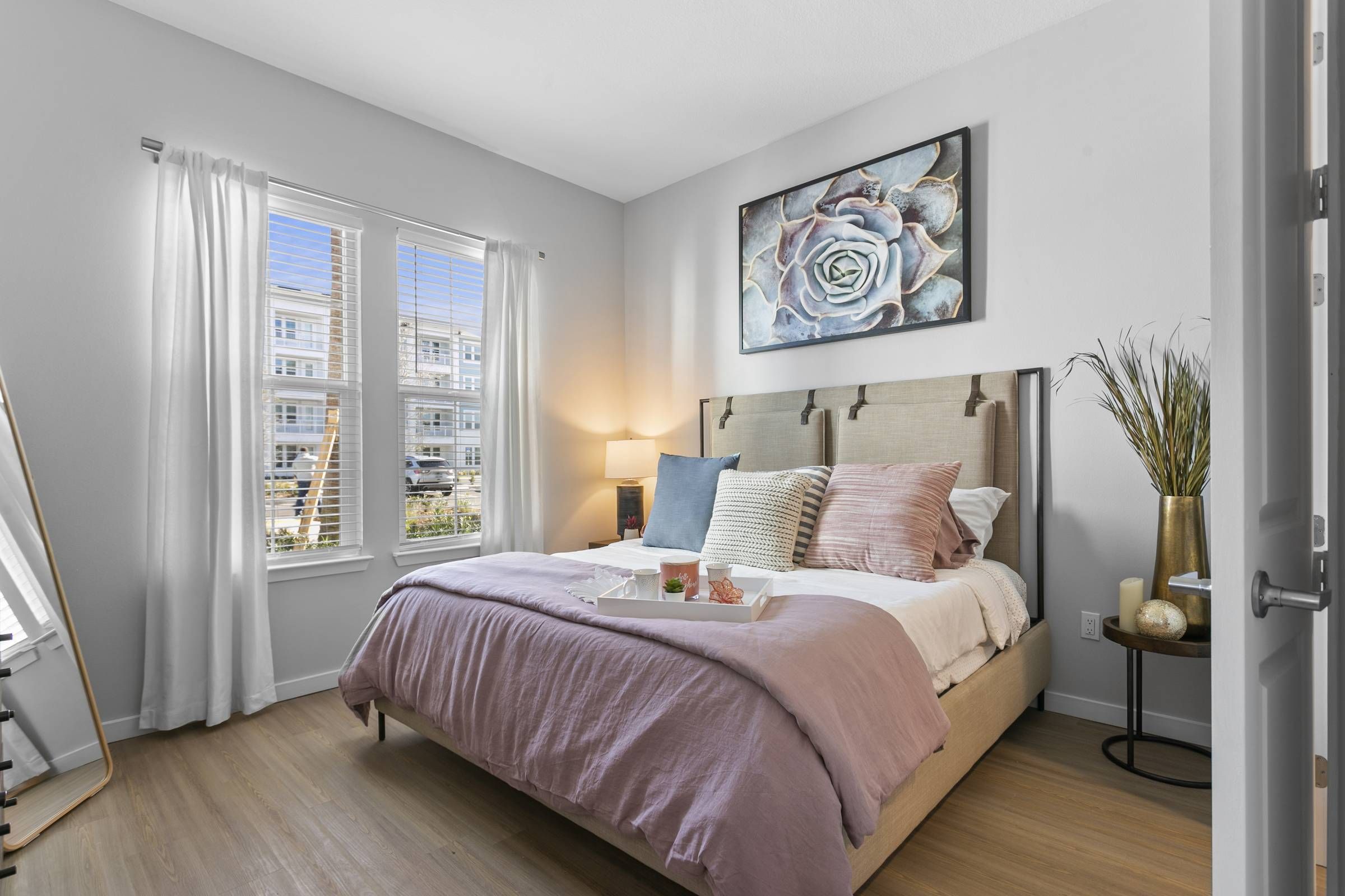 The bedroom at Alta Belleair, showcasing a comfortable bed with pastel bedding, a large window for natural light, and elegant artwork above the headboard.